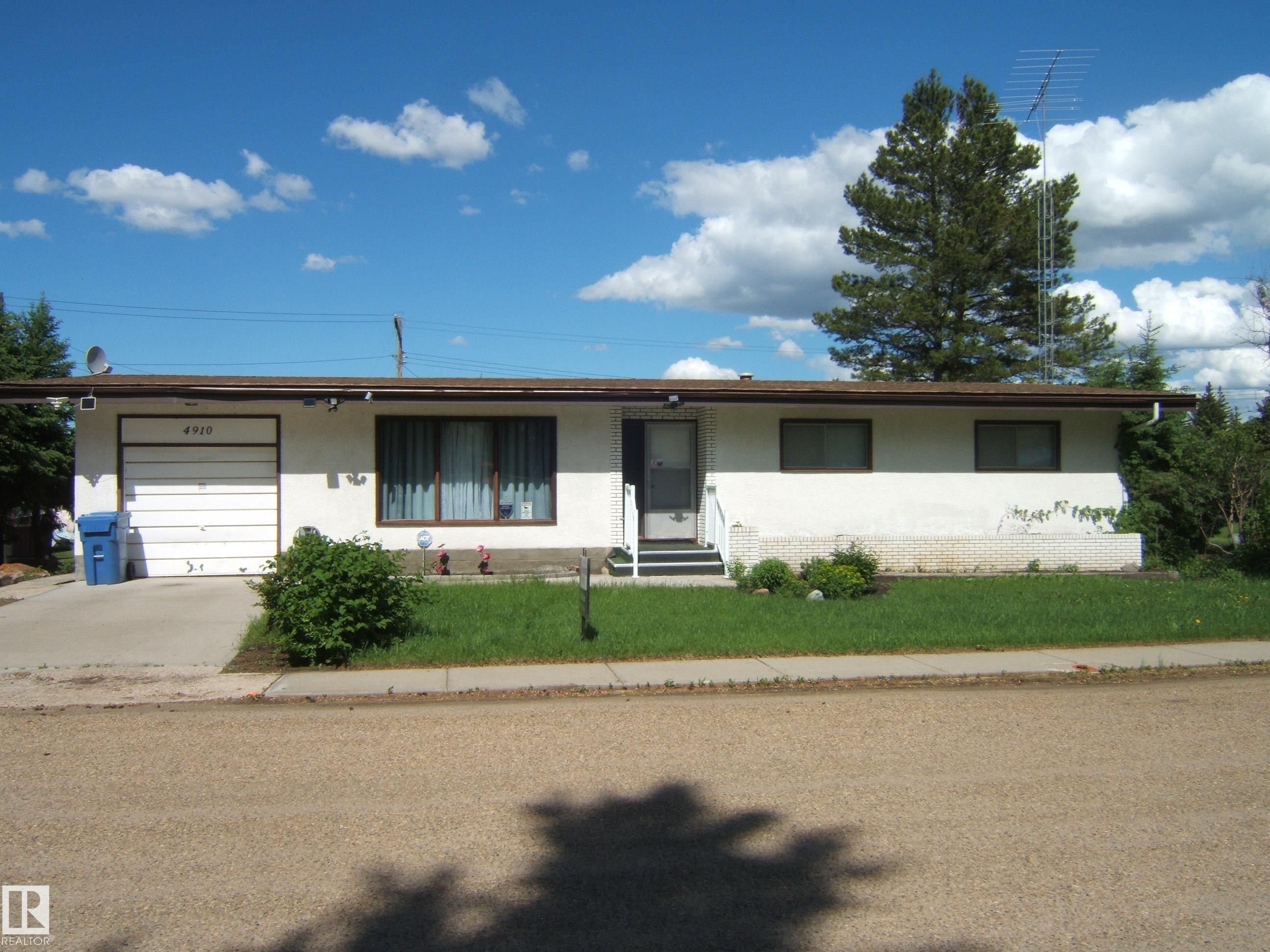 White exterior with an attached garage, paved driveway, and mature landscaping - 4910 53 Avenue, Willingdon, AB