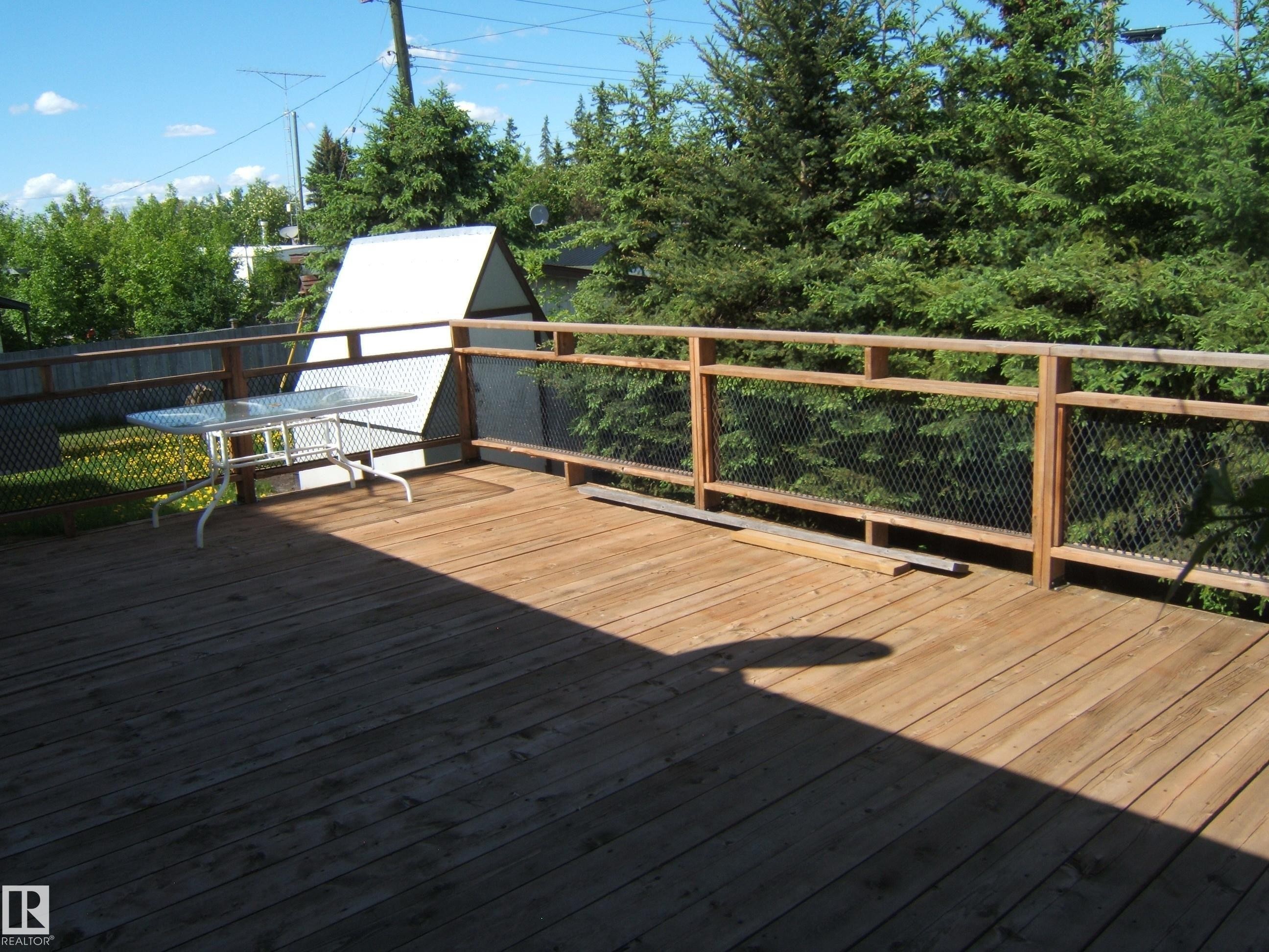 Expansive wood deck with wood and mesh railing, featuring surrounding mature trees - 4910 53 Avenue, Willingdon, AB
