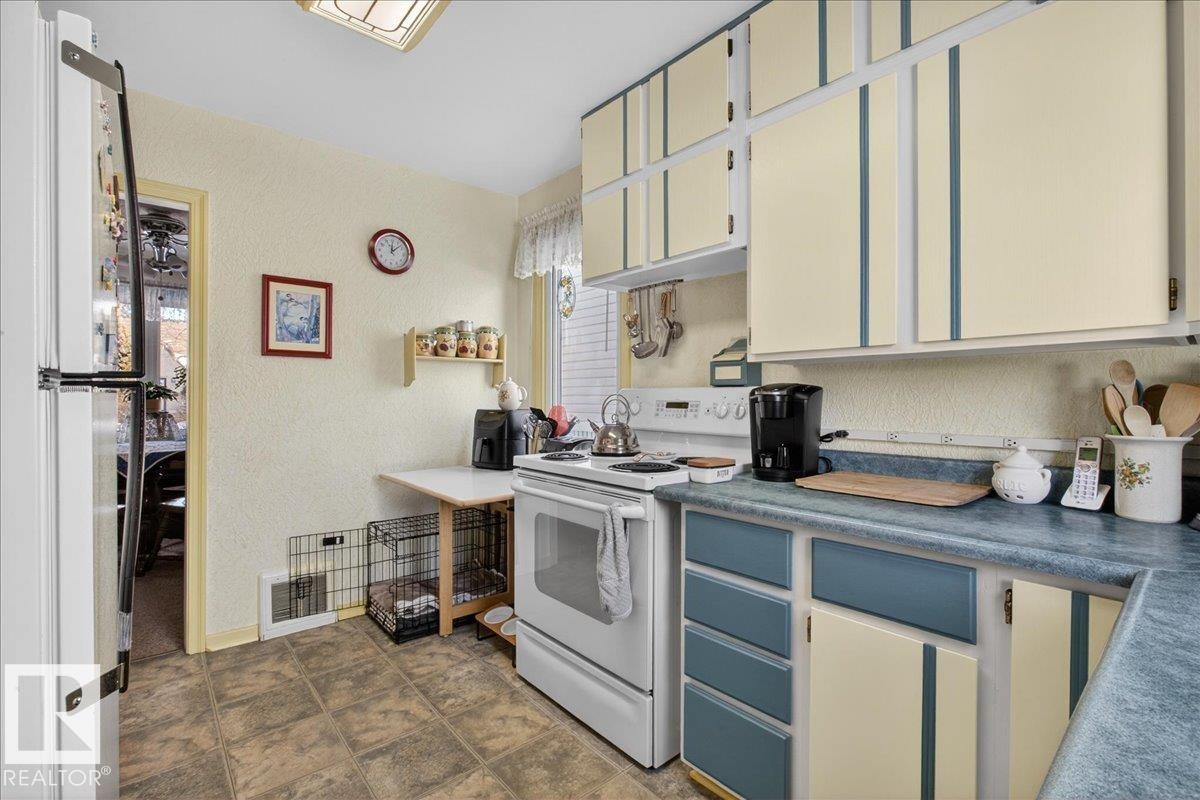 Kitchen featuring white appliances, a textured wall, blue cabinetry, and dark countertops - 11630 71 Street, Edmonton, AB - Indoor Photo Showing Kitchen