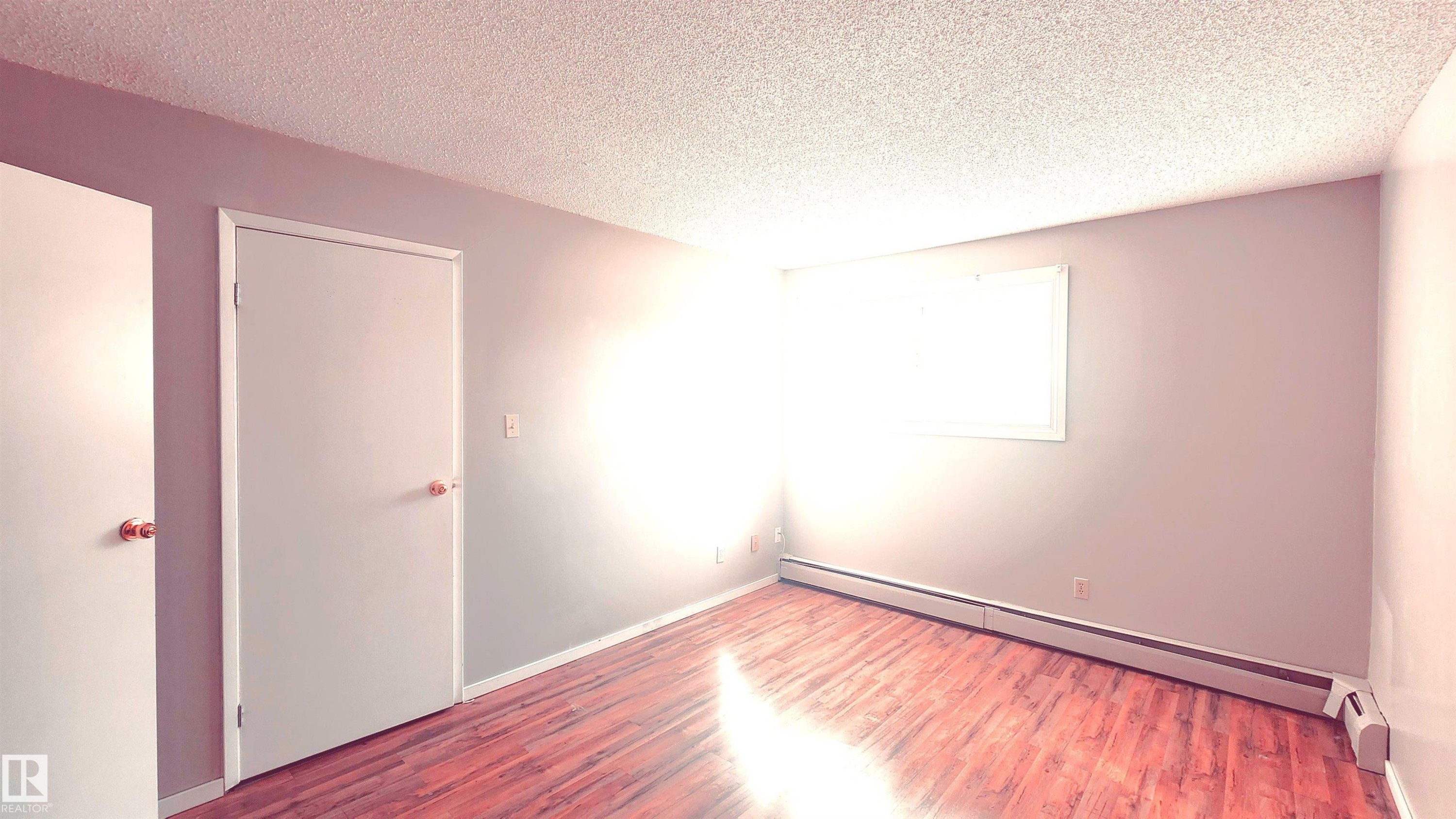 Unfurnished room featuring wood finished floors, a textured ceiling, and a baseboard heating unit - 2 11265 31 Avenue, Edmonton, AB - Indoor Photo Showing Other Room
