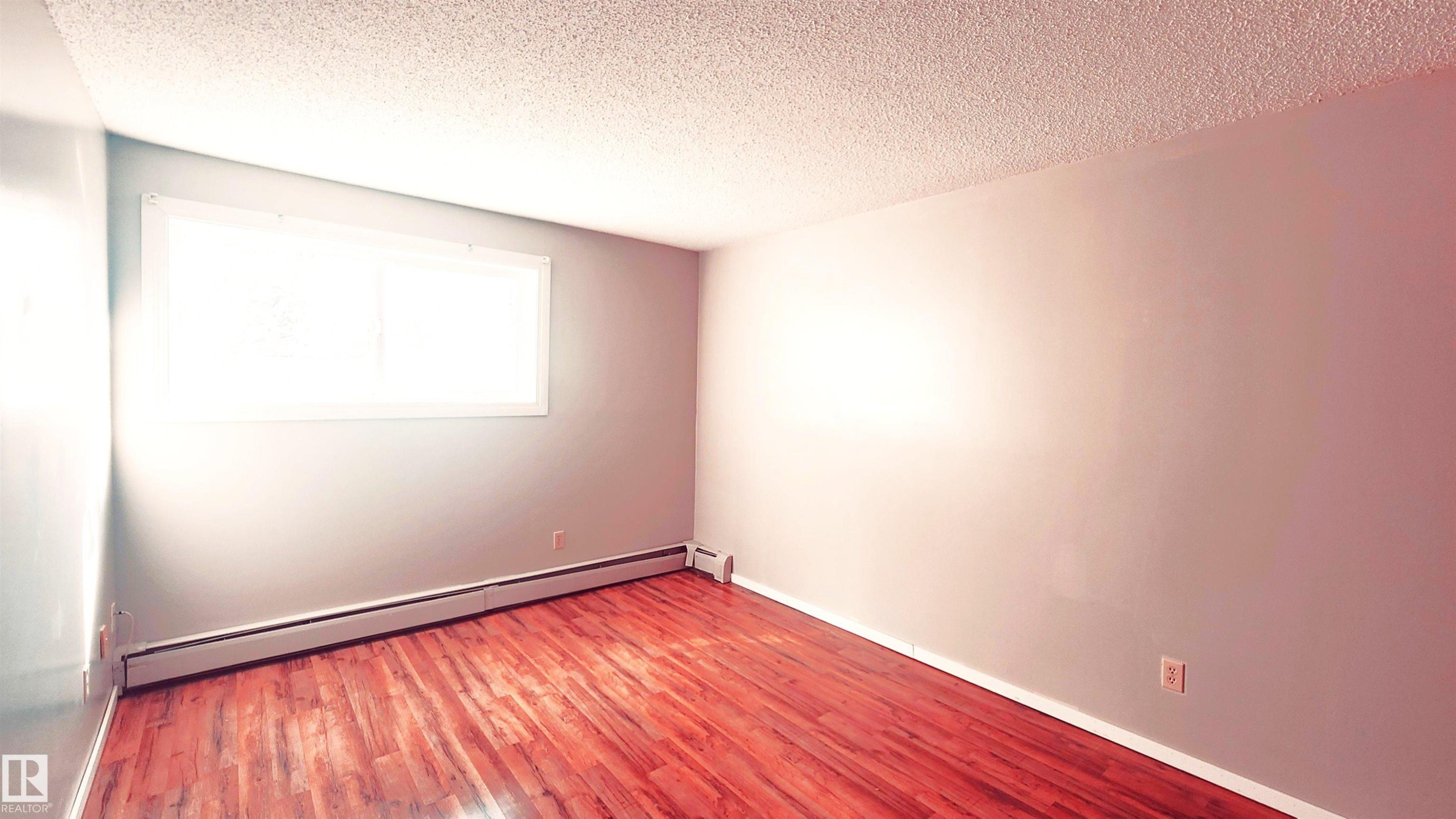 Unfurnished room with wood finished floors, a textured ceiling, and baseboard heating - 2 11265 31 Avenue, Edmonton, AB - Indoor Photo Showing Other Room
