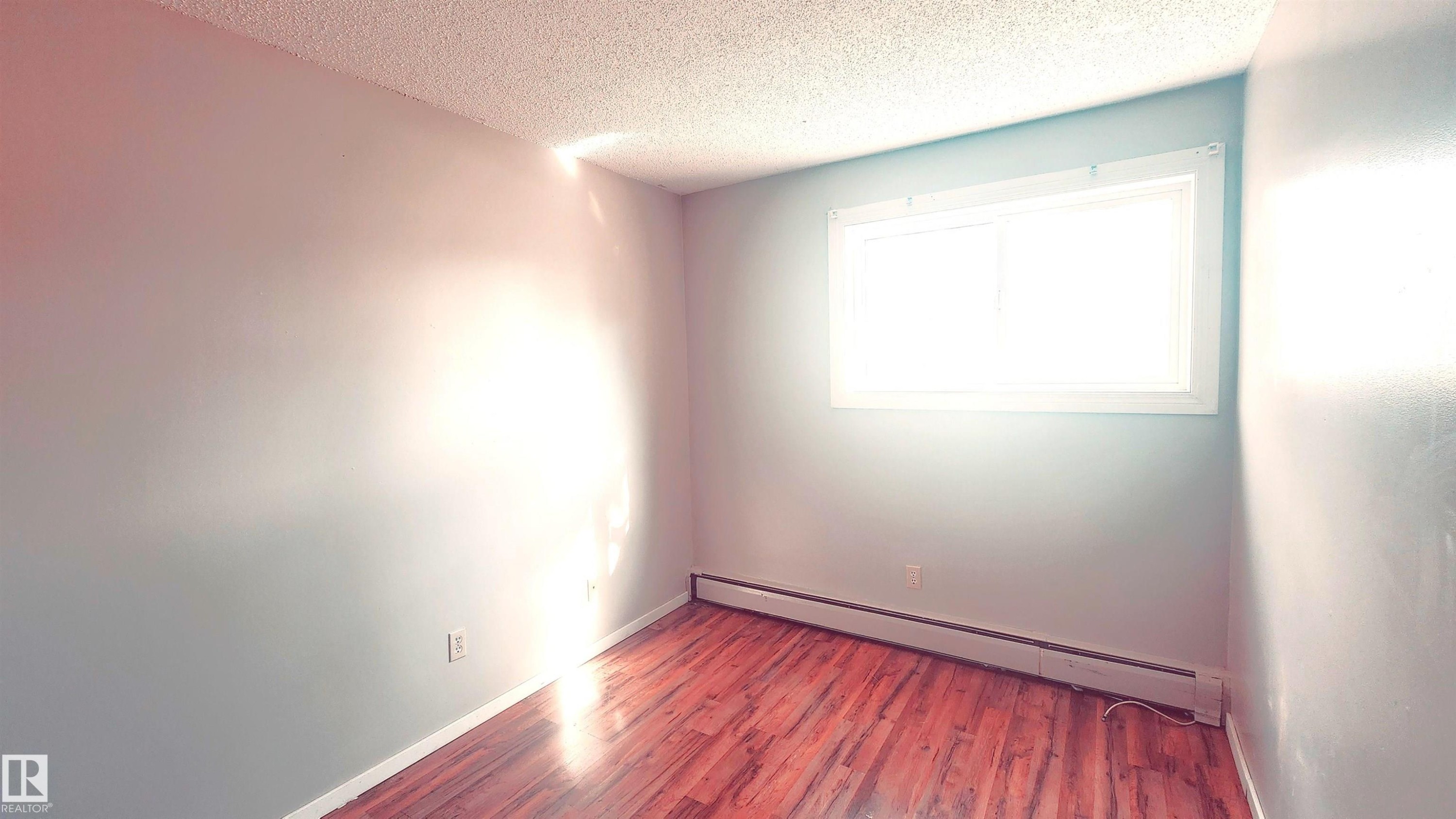Unfurnished room with a baseboard radiator, a textured ceiling, and wood finished floors - 2 11265 31 Avenue, Edmonton, AB - Indoor Photo Showing Other Room
