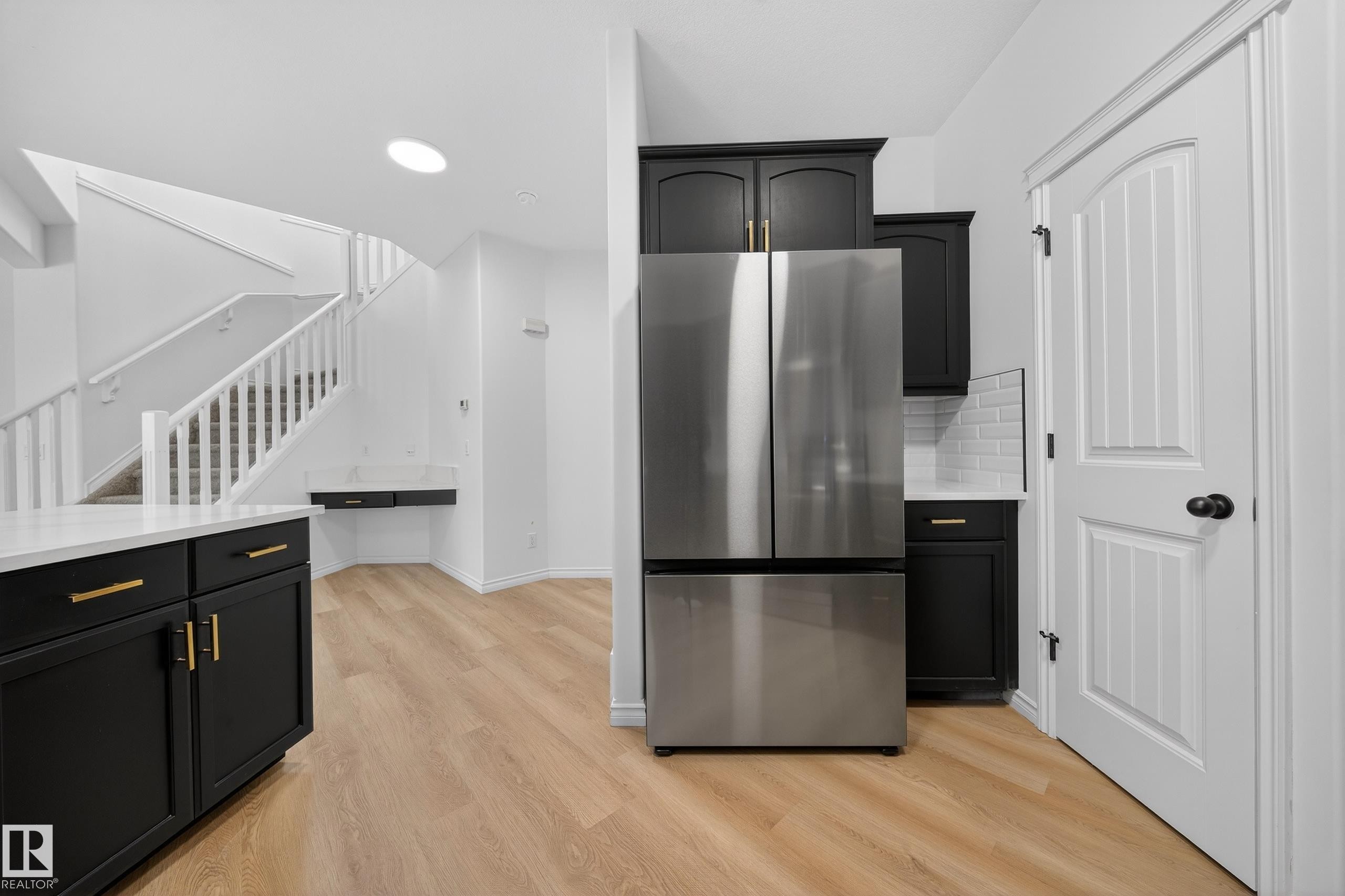 Kitchen featuring dark cabinets, freestanding refrigerator, light wood-type flooring, light stone counters, and backsplash - 1741 63A Street, Edmonton, AB - Indoor