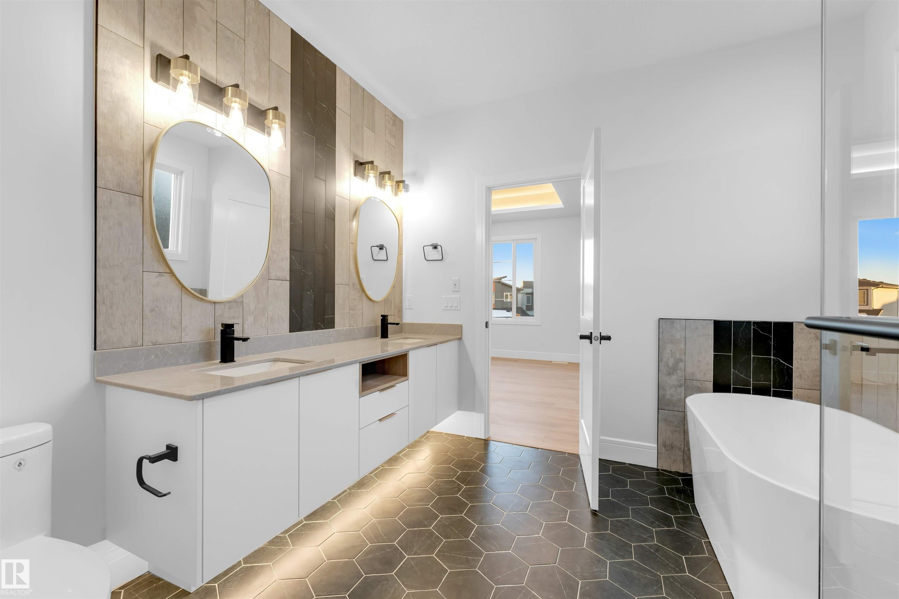 Bathroom with a soaking tub, double vanity, dark tile patterned flooring, and tile walls - 150 Creekside Lane, Leduc, AB - Indoor Photo Showing Bathroom
