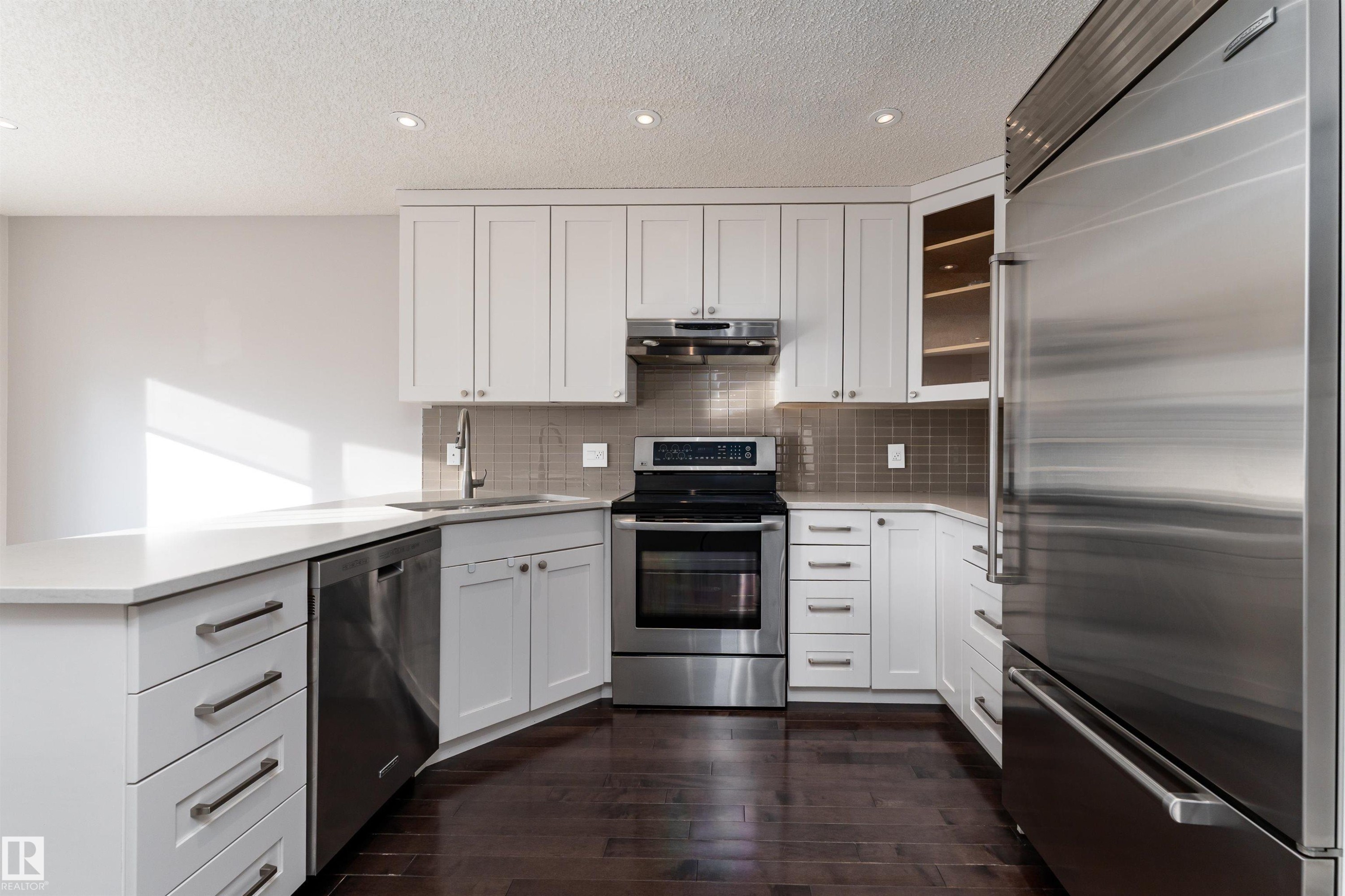 Kitchen with appliances with stainless steel finishes, white cabinetry, a peninsula, dark wood-style floors, and under cabinet range hood - 174 Oeming Road, Edmonton, AB - Indoor Photo Showing Kitchen With Upgraded Kitchen