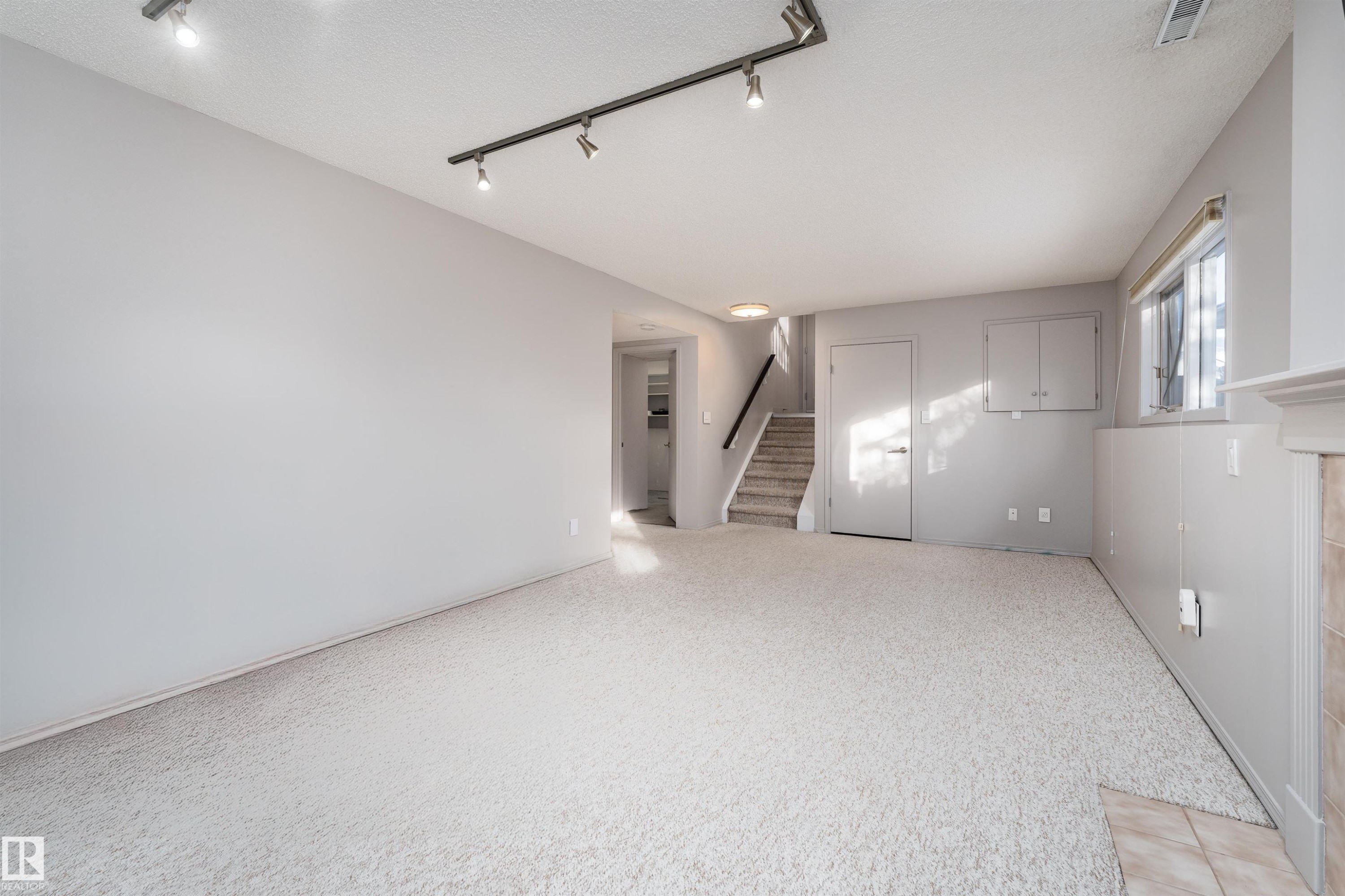 Unfurnished living room with track lighting, stairs, and light carpet - 174 Oeming Road, Edmonton, AB - Indoor Photo Showing Other Room