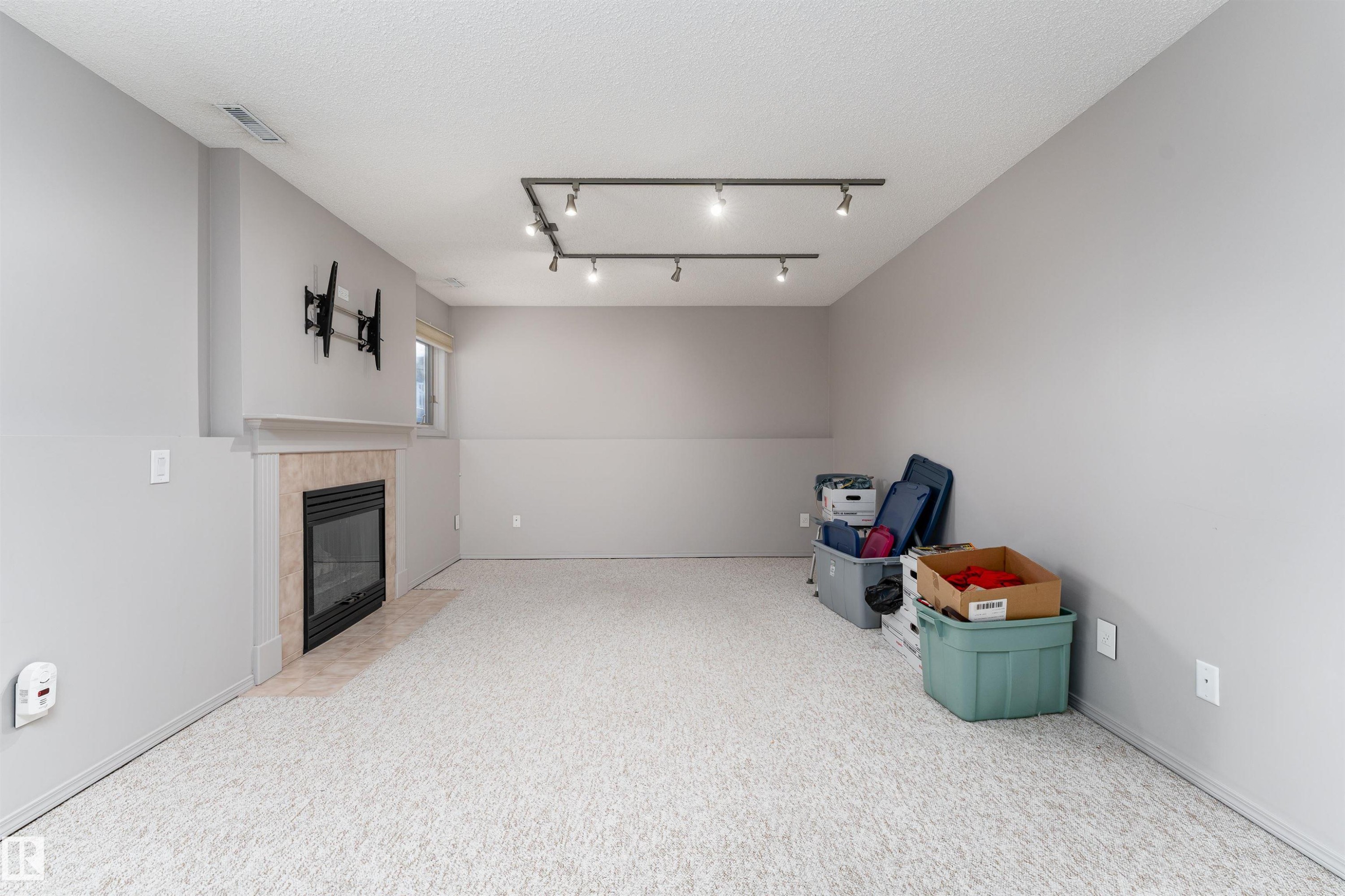 Below grade area featuring a tile fireplace, carpet flooring, track lighting, and a textured ceiling - 174 Oeming Road, Edmonton, AB - Indoor Photo Showing Other Room With Fireplace