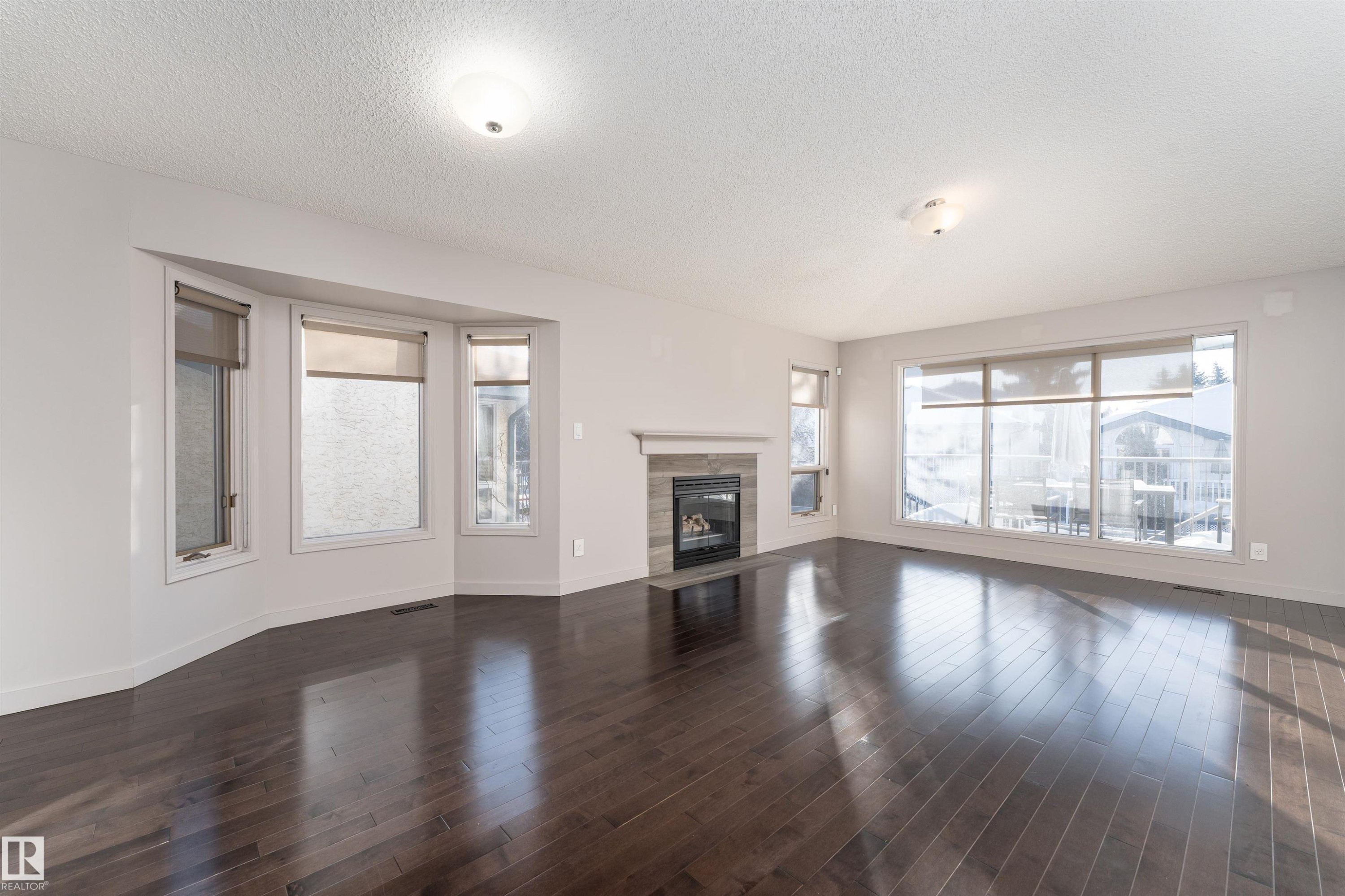 Unfurnished living room featuring a textured ceiling, a tiled fireplace, and dark wood-type flooring - 174 Oeming Road, Edmonton, AB - Indoor Photo Showing Living Room With Fireplace