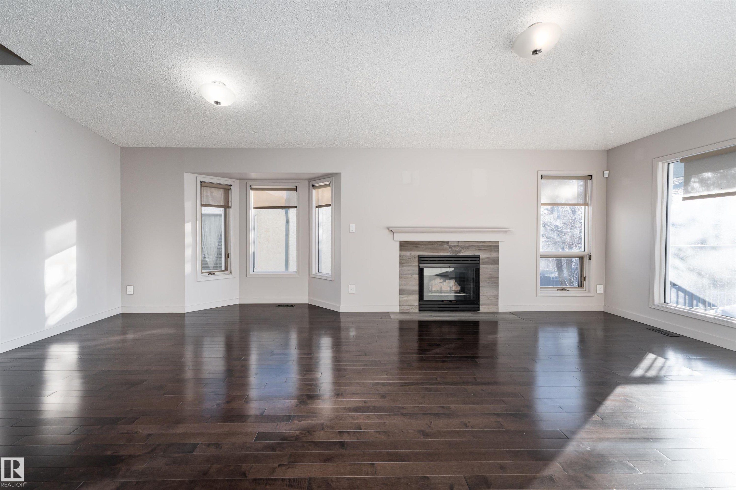 Unfurnished living room with a textured ceiling, a tile fireplace, plenty of natural light, and dark wood-type flooring - 174 Oeming Road, Edmonton, AB - Indoor Photo Showing Living Room With Fireplace