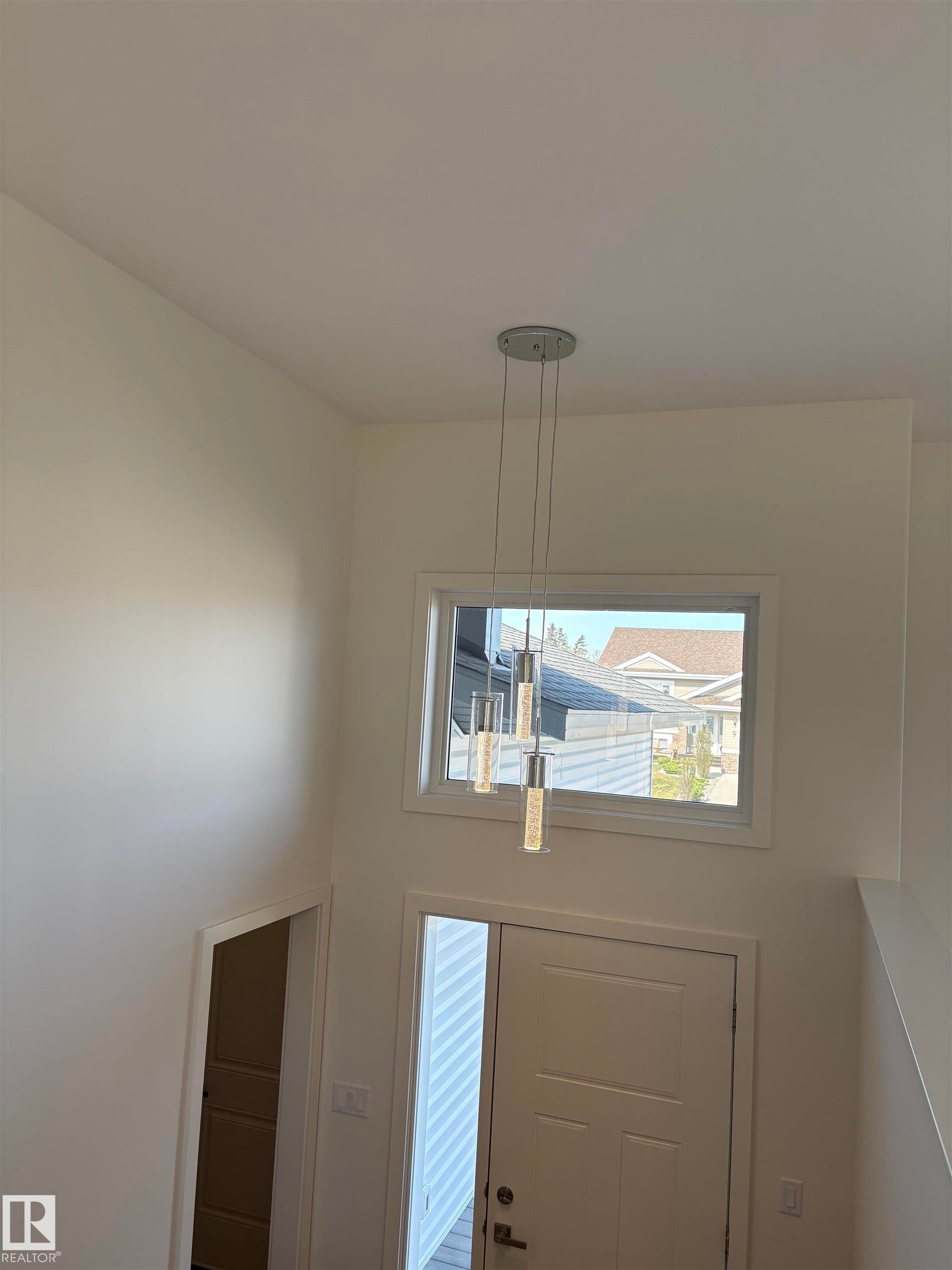 Two-story foyer featuring an upper window, a contemporary multi-pendant chandelier, and a white paneled entry door with side lite - 6 4 Avenue, Hay Lakes, AB