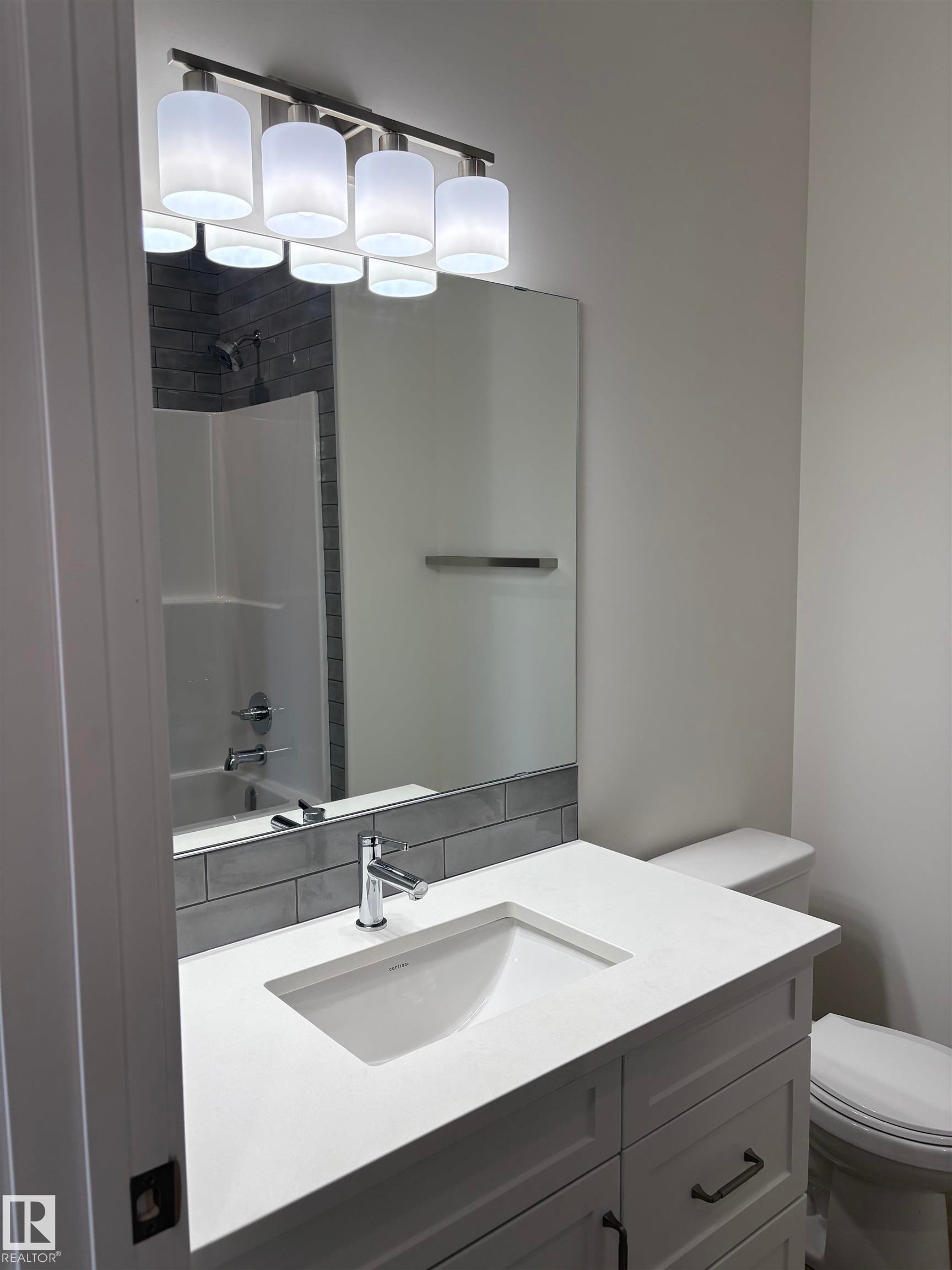 Bathroom vanity featuring a white countertop with an integrated sink, polished chrome faucet, and white shaker-style cabinetry with dark hardware - 6 4 Avenue, Hay Lakes, AB