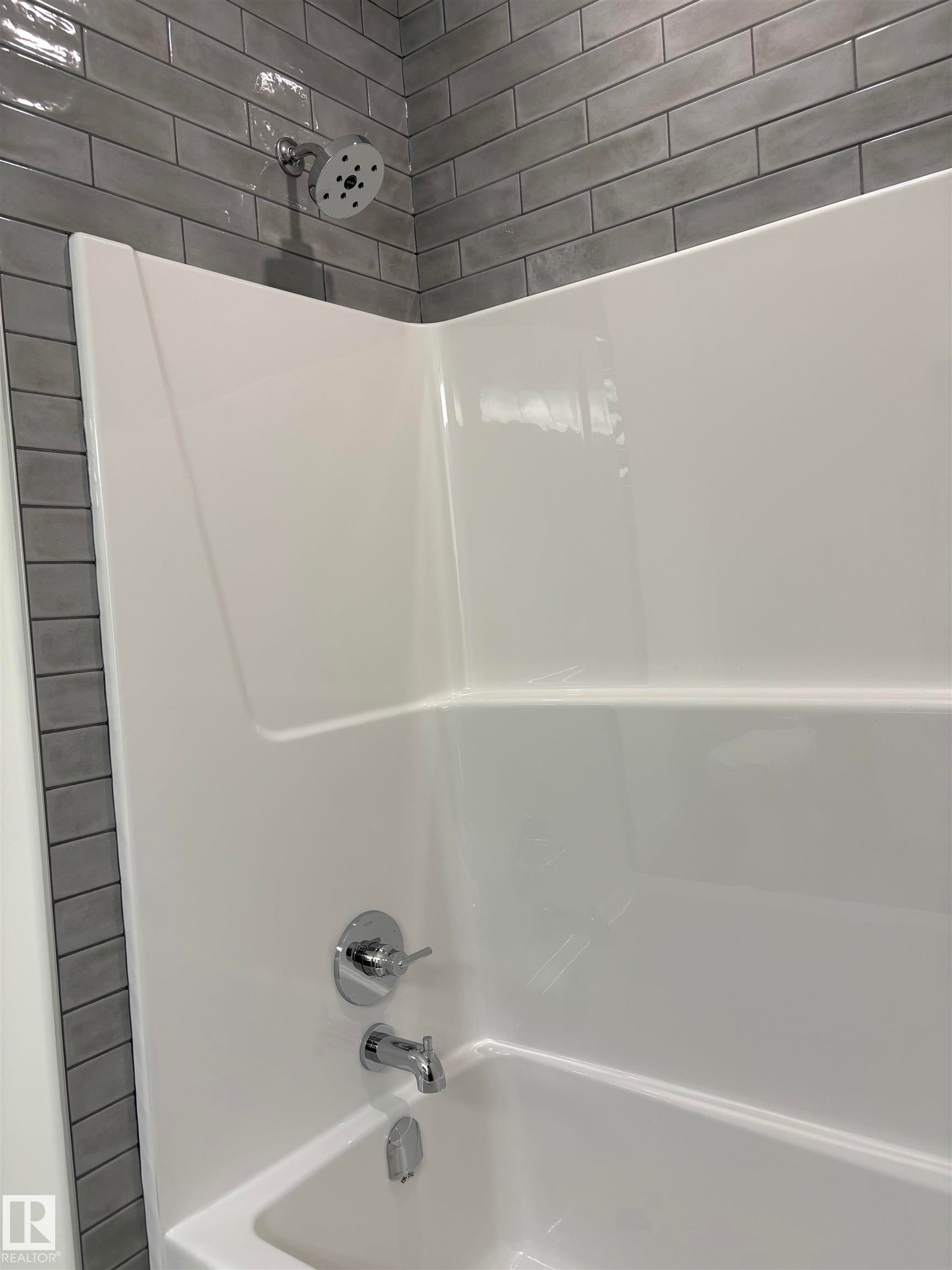 Bathtub with integrated shower surround, featuring gray subway tile shower walls, a chrome showerhead, and a chrome tub spout with matching controls - 6 4 Avenue, Hay Lakes, AB