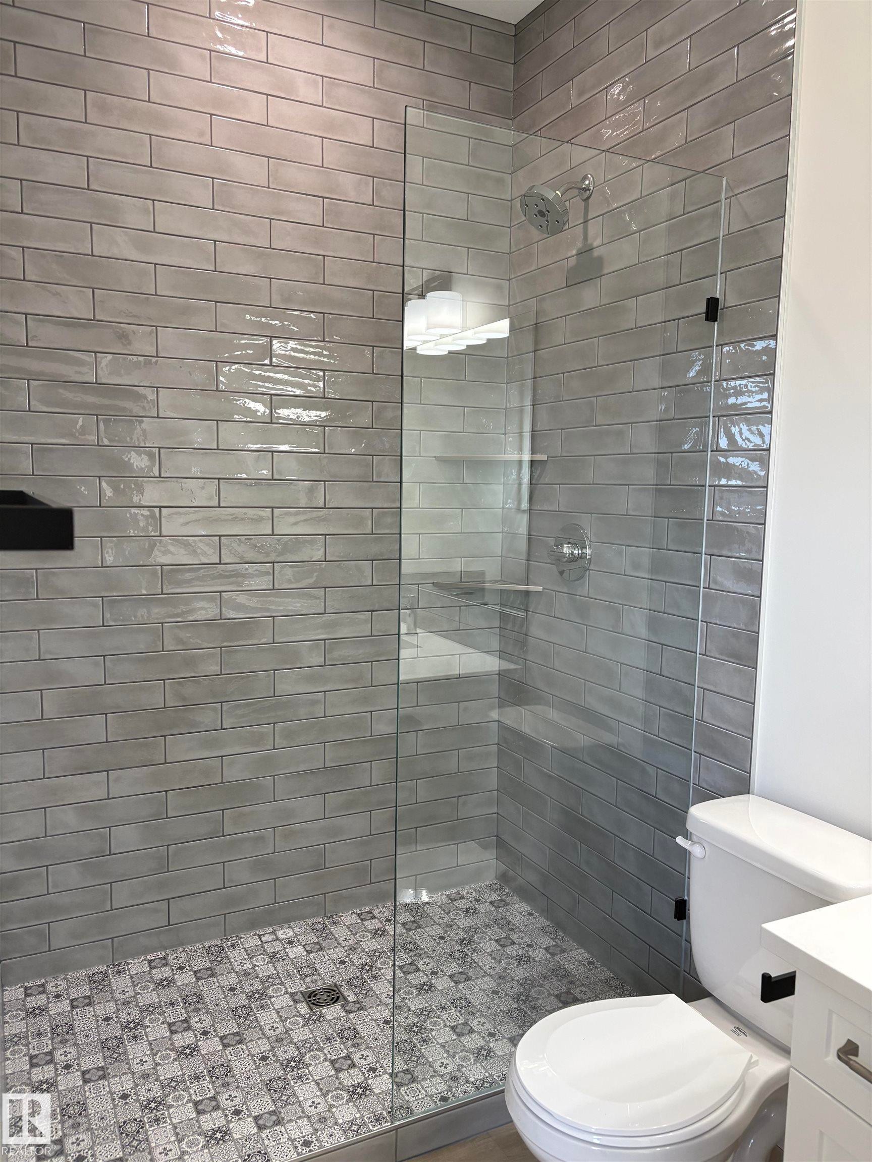 Tiled shower enclosure featuring a clear glass panel, gray subway wall tiles, and a patterned tile shower floor - 6 4 Avenue, Hay Lakes, AB