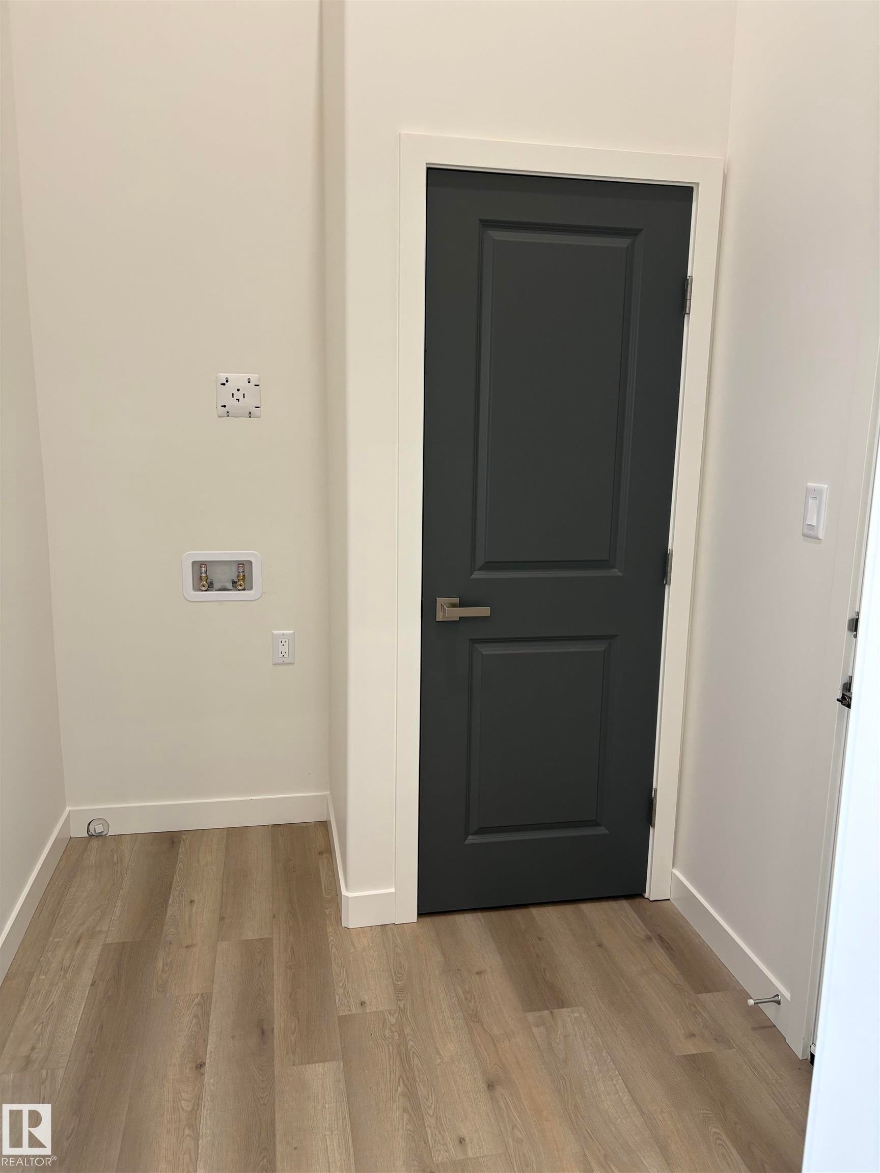 Laundry area with light wood-finish flooring, white baseboards, and a dark paneled door with brushed nickel hardware - 6 4 Avenue, Hay Lakes, AB