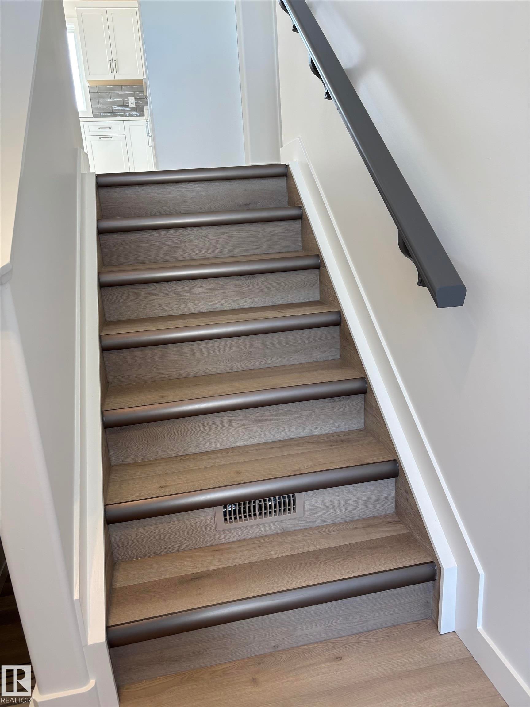Staircase featuring wood-finish treads with dark-toned nosing, white wall paneling, and a dark wall-mounted handrail - 6 4 Avenue, Hay Lakes, AB