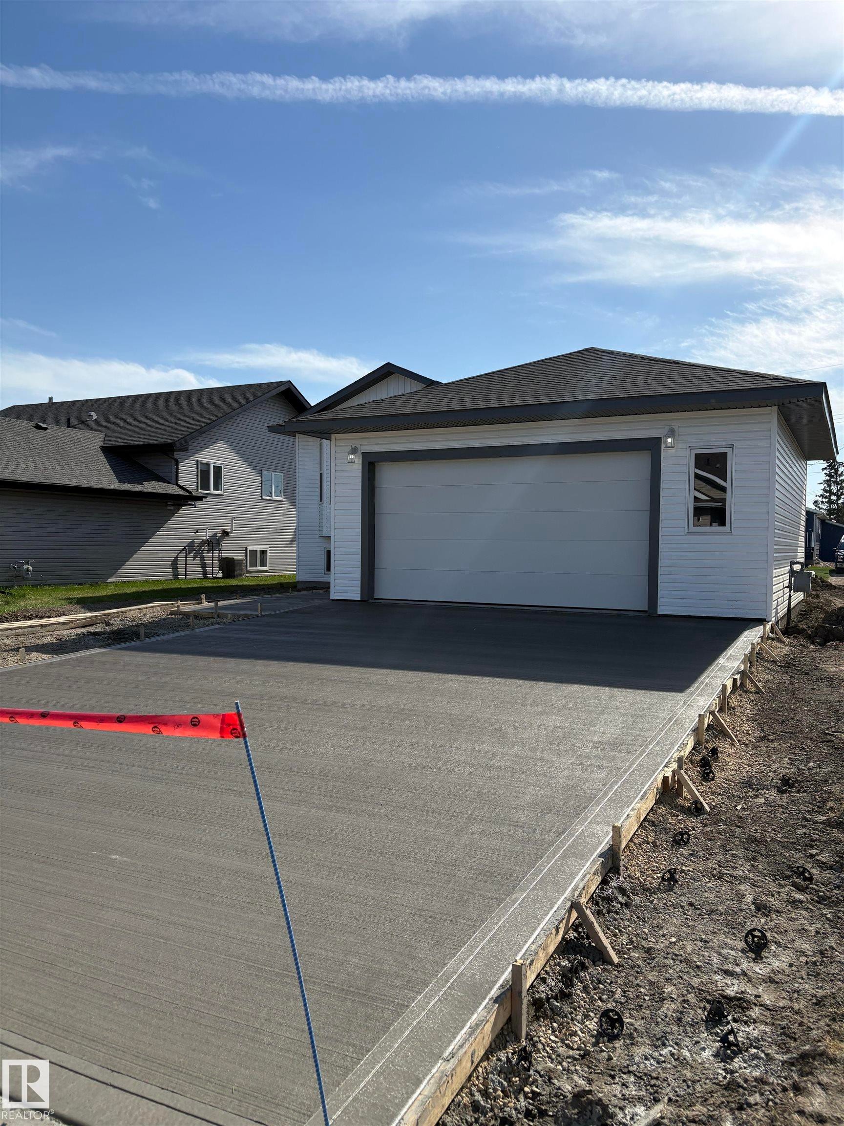 Exterior facade featuring white siding, a dark asphalt shingle roof, and an attached garage with a light-colored door - 6 4 Avenue, Hay Lakes, AB