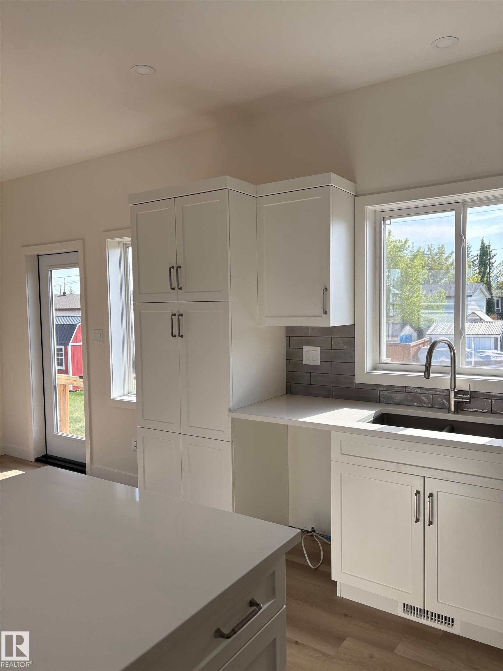 Kitchen featuring white cabinetry with dark hardware, a white kitchen island, light wood-finish flooring, and a window above the sink - 6 4 Avenue, Hay Lakes, AB