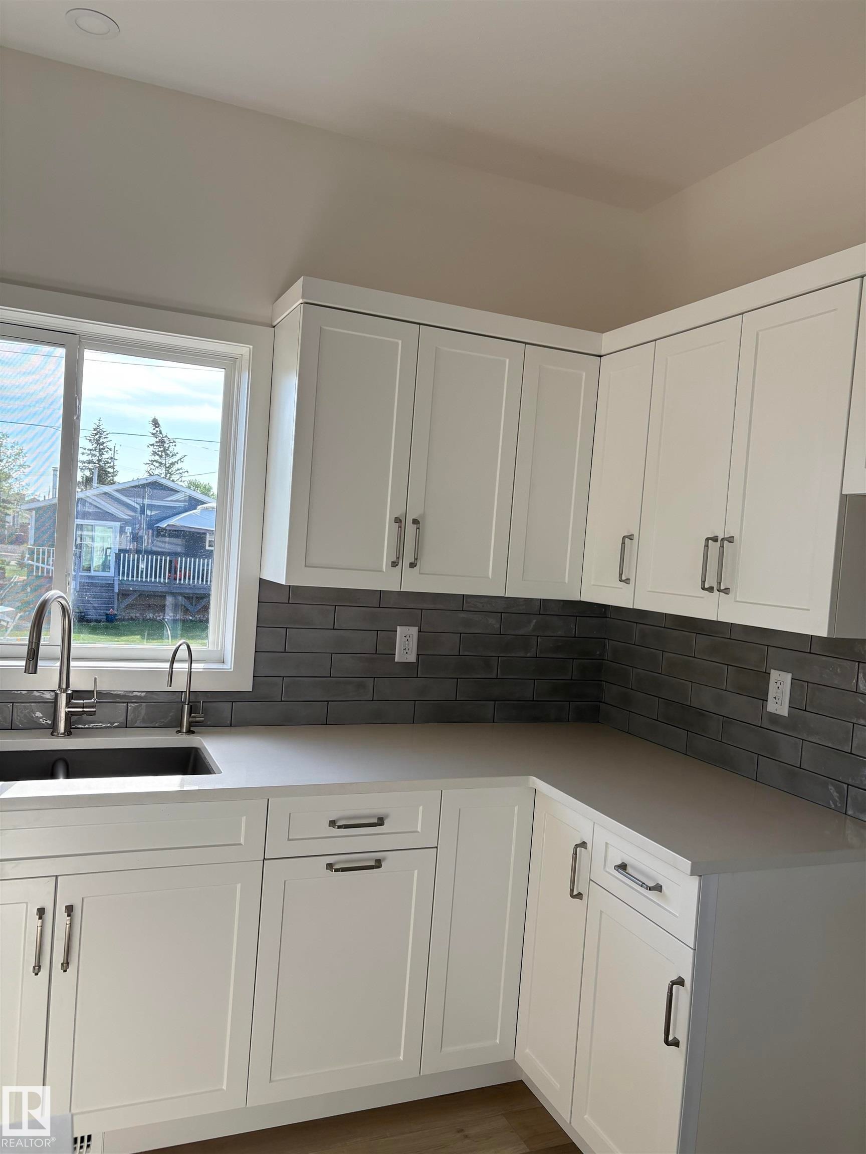 Modern kitchen featuring white shaker-style cabinetry, light-toned countertops, and a gray subway tile backsplash - 6 4 Avenue, Hay Lakes, AB