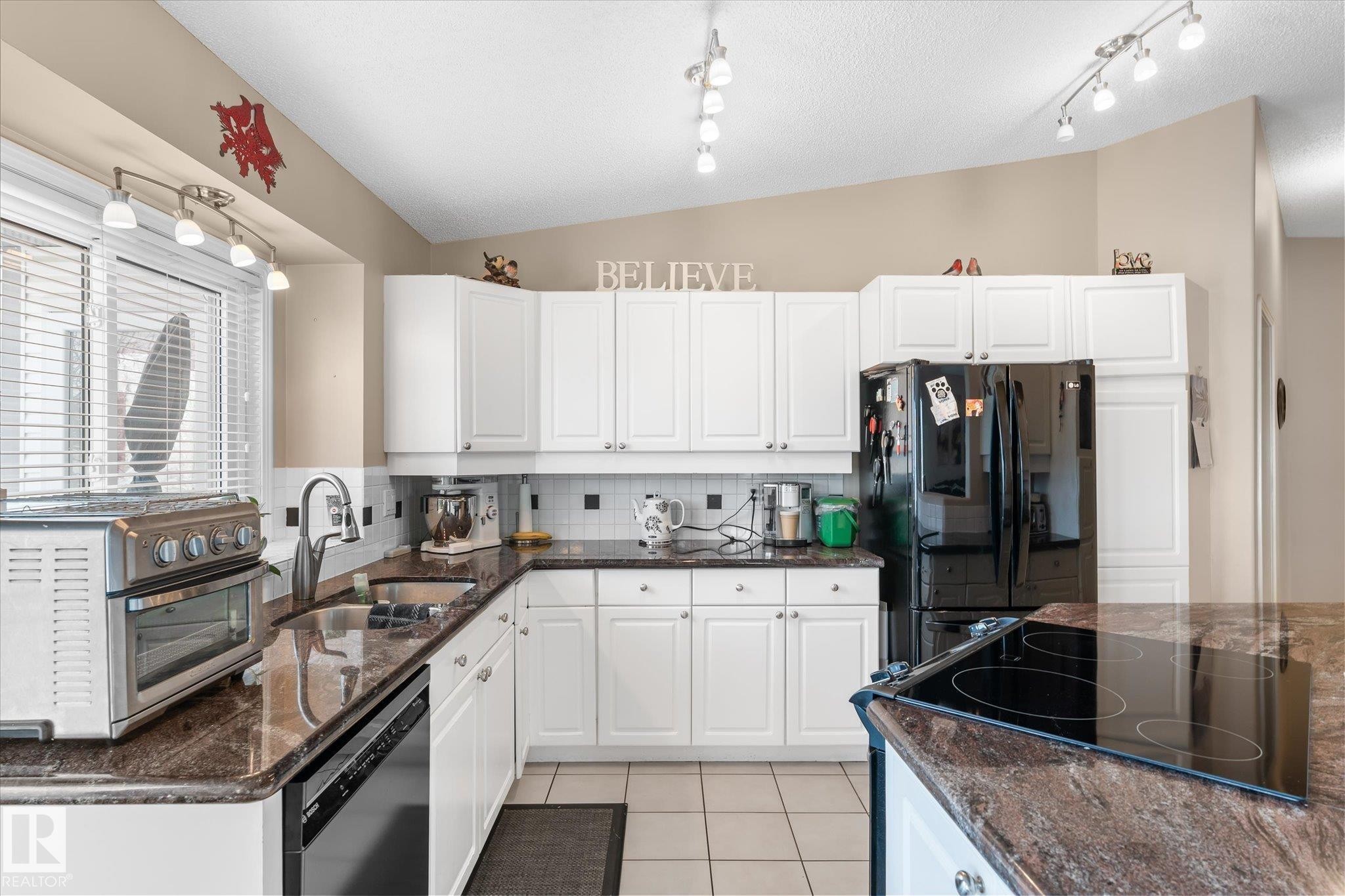 Kitchen with black appliances, dark stone counters, white cabinets, tasteful backsplash, and lofted ceiling - 7020 157 Avenue, Edmonton, AB - Indoor Photo Showing Kitchen With Double Sink