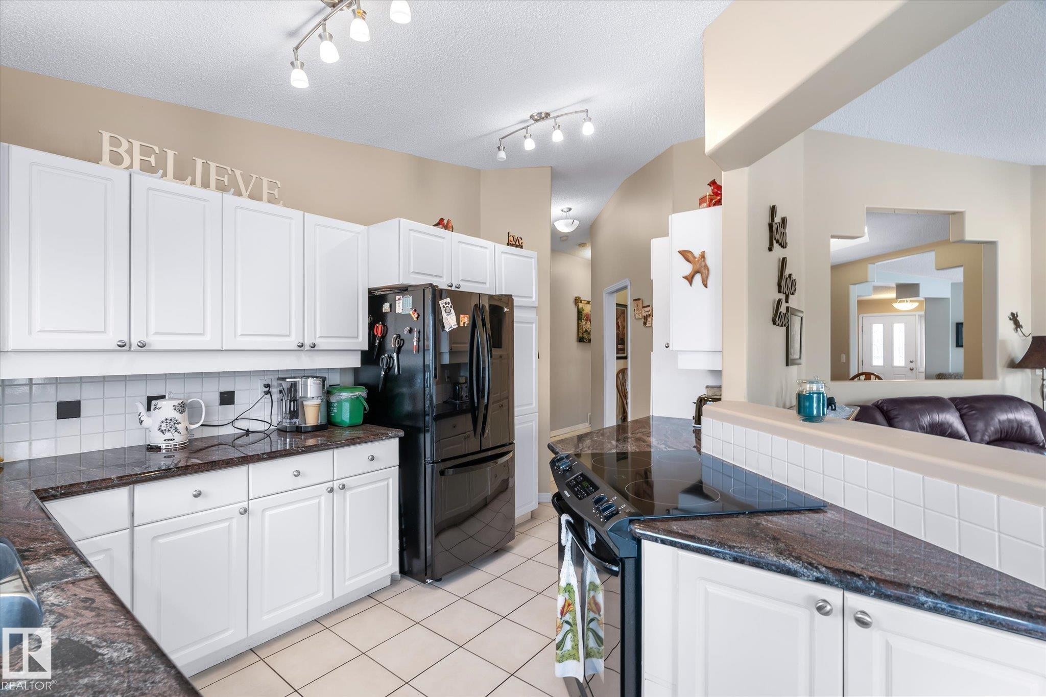 Kitchen with tasteful backsplash, white cabinetry, black appliances, dark stone countertops, and light tile patterned flooring - 7020 157 Avenue, Edmonton, AB - Indoor Photo Showing Kitchen