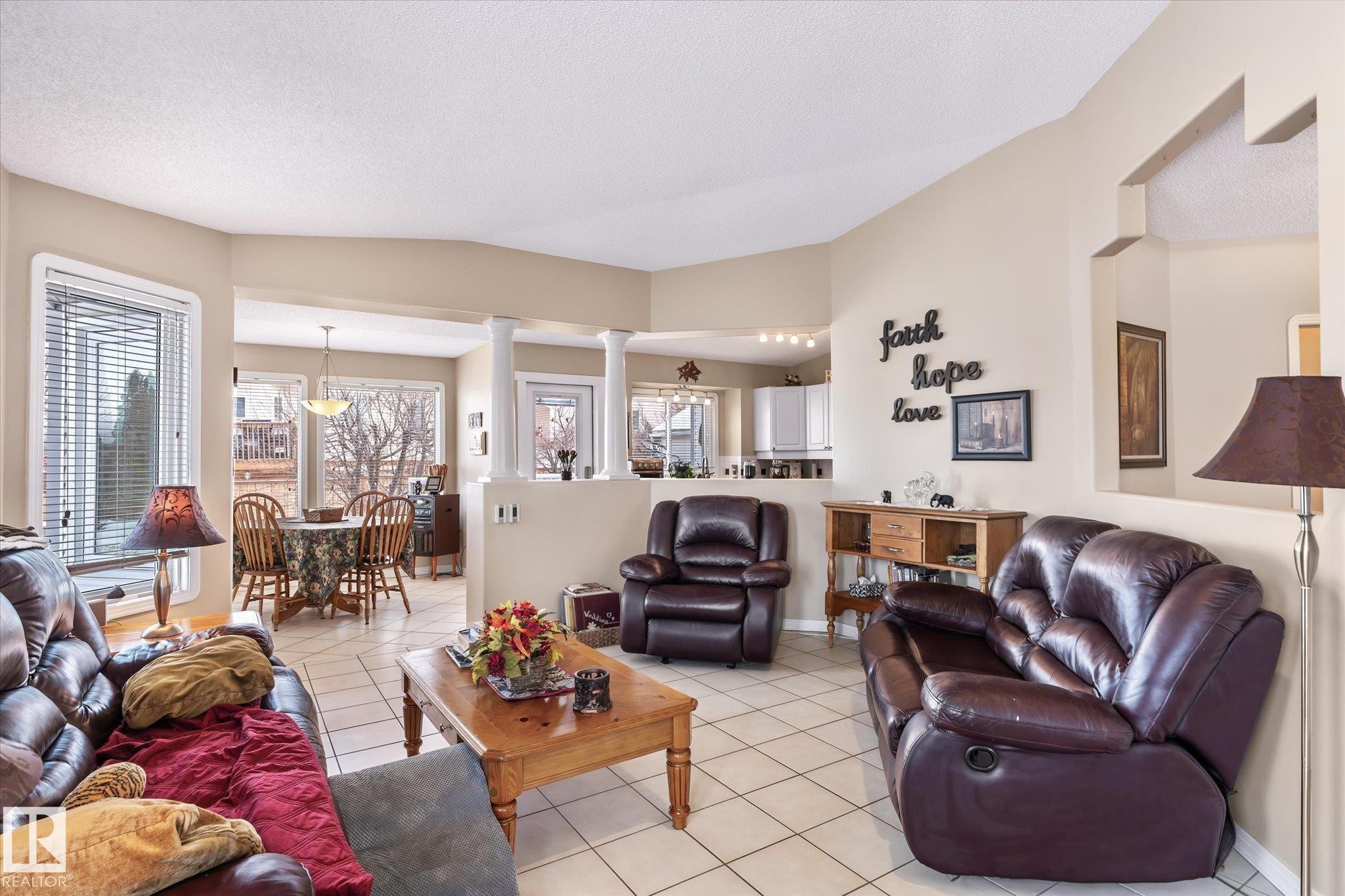 Living area featuring light tile patterned floors, vaulted ceiling, a textured ceiling, and decorative columns - 7020 157 Avenue, Edmonton, AB - Indoor Photo Showing Living Room