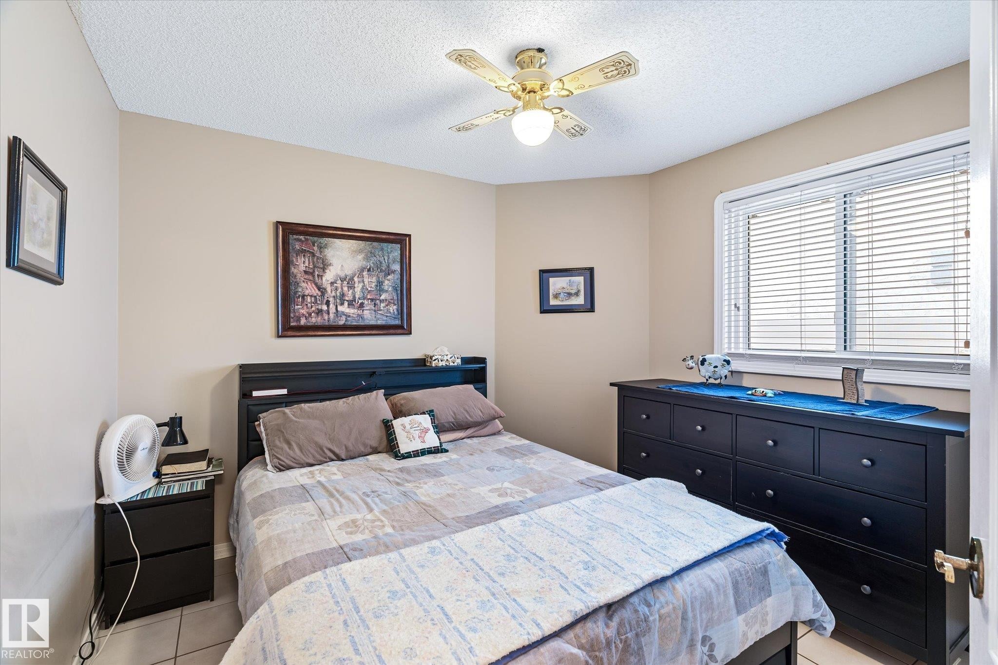 Bedroom featuring a textured ceiling, light tile patterned floors, and a ceiling fan - 7020 157 Avenue, Edmonton, AB - Indoor Photo Showing Bedroom