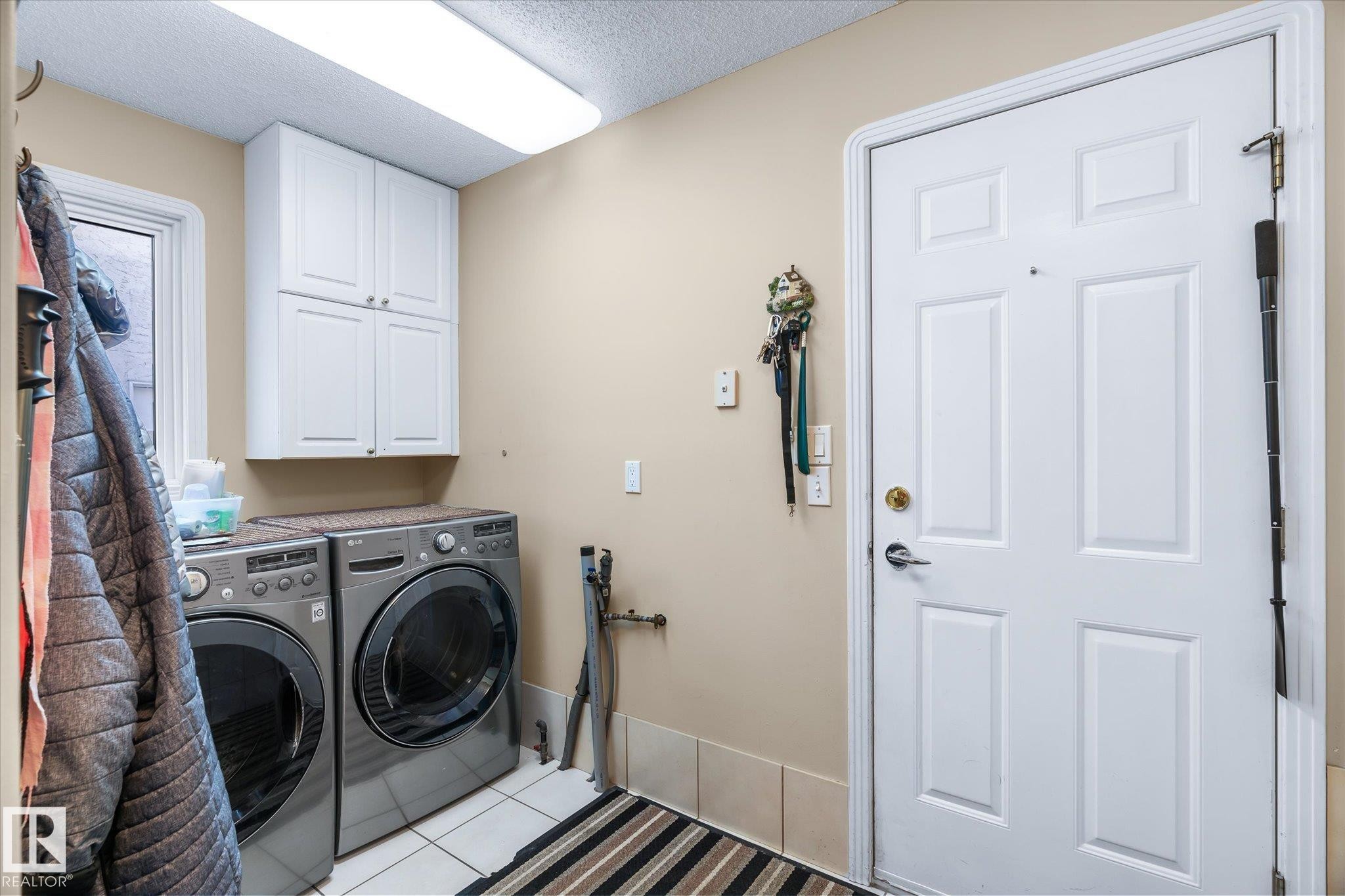 Laundry room featuring cabinet space, tile patterned flooring, a textured ceiling, and separate washer and dryer - 7020 157 Avenue, Edmonton, AB - Indoor Photo Showing Laundry Room