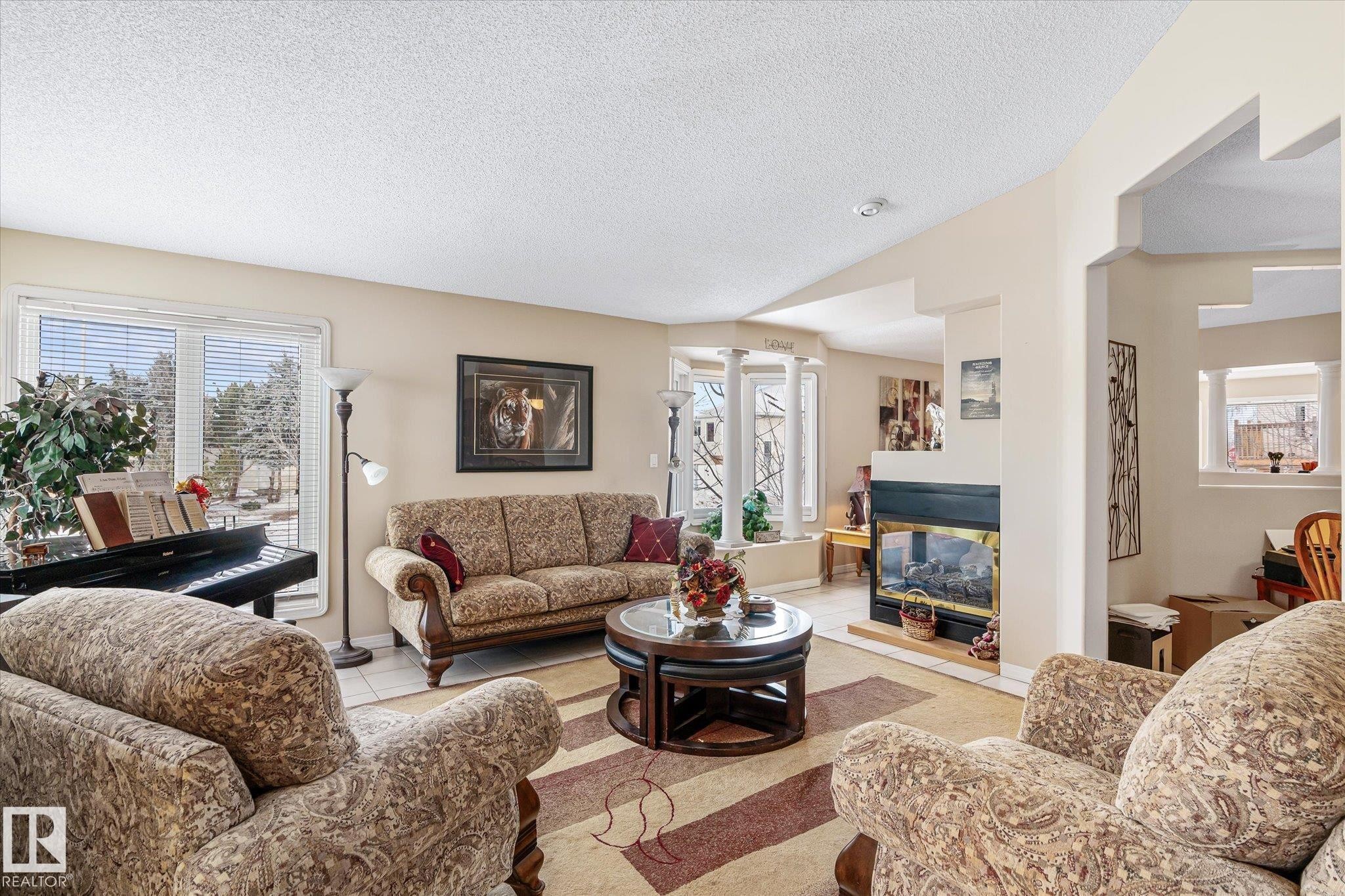 Tiled living room featuring a textured ceiling, healthy amount of natural light, and a multi sided fireplace - 7020 157 Avenue, Edmonton, AB - Indoor Photo Showing Living Room