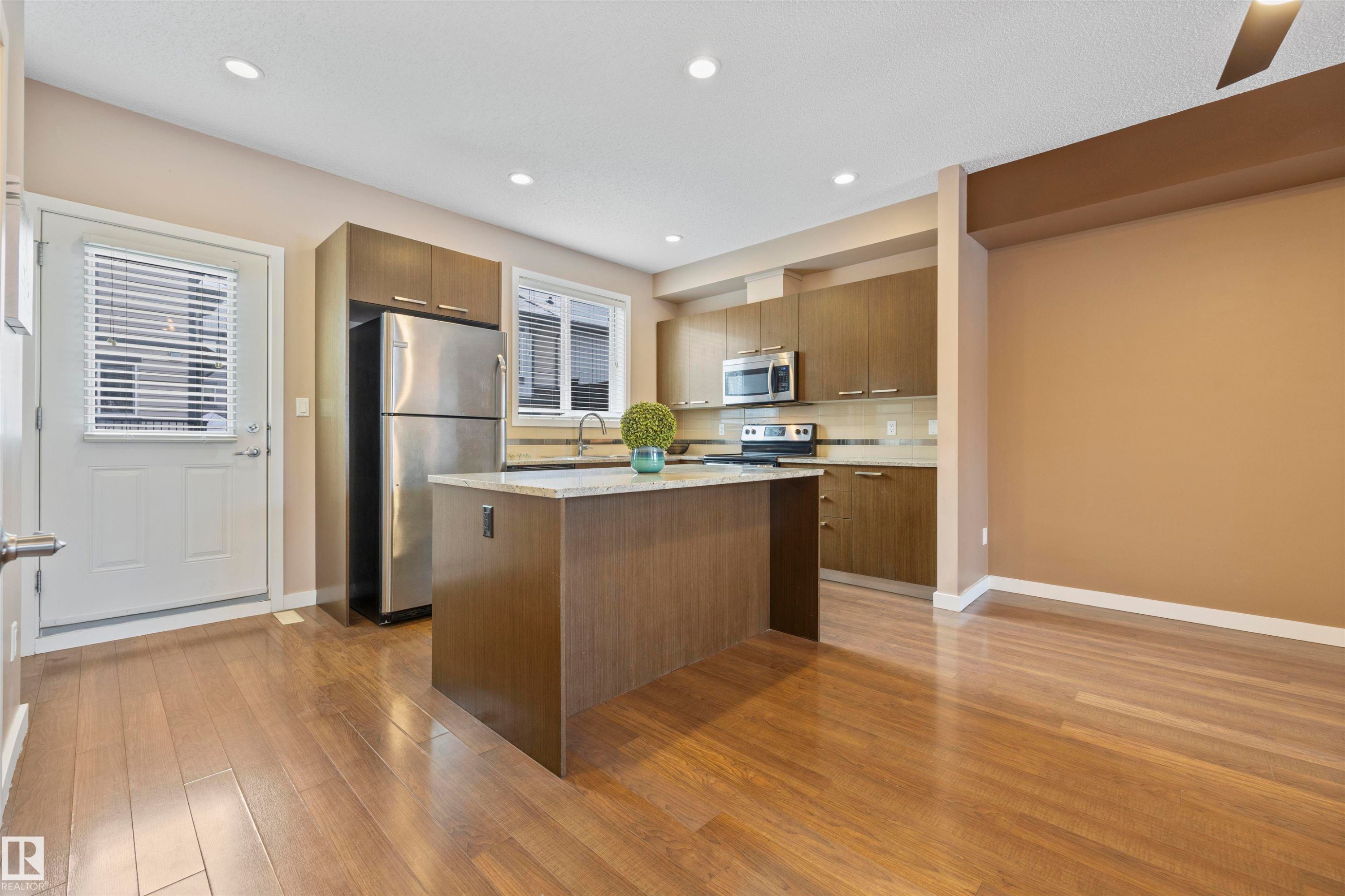 Kitchen with a center island, appliances with stainless steel finishes, light stone counters, light wood finished floors, and modern cabinets - 56 655 Watt Boulevard, Edmonton, AB - Indoor Photo Showing Kitchen