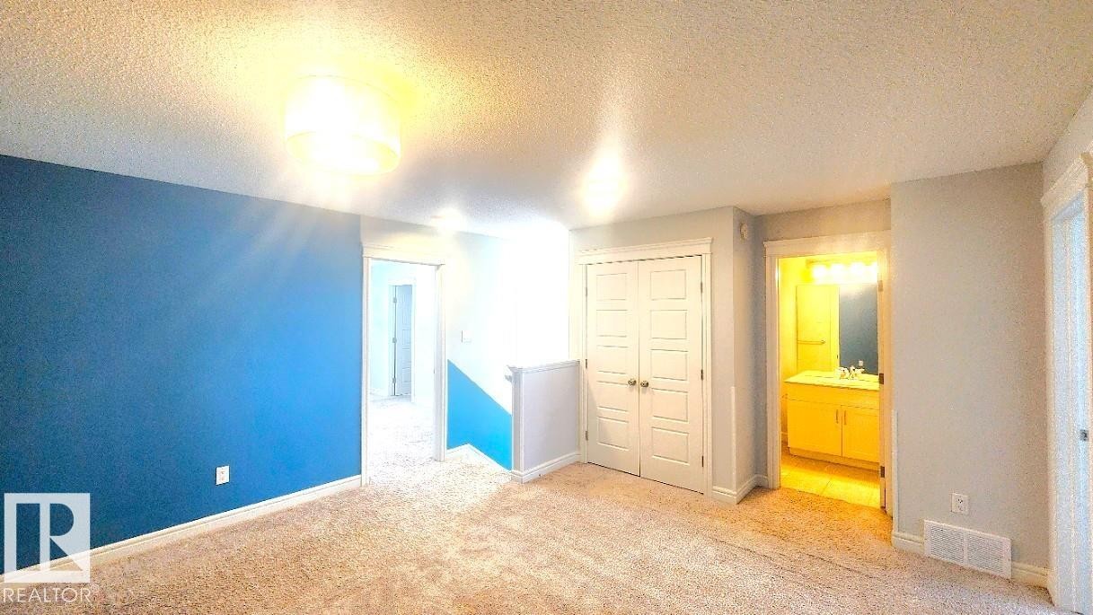 Unfurnished bedroom featuring a textured ceiling, light colored carpet, a closet, and ensuite bathroom - 4610 Kinsella Landing Sw, Edmonton, AB - Indoor