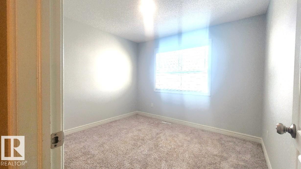 Carpeted spare room featuring a textured ceiling and baseboards - 4610 Kinsella Landing Sw, Edmonton, AB - Indoor Photo Showing Other Room