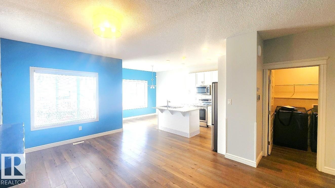 Kitchen with white cabinetry, a kitchen island with sink, a kitchen breakfast bar, appliances with stainless steel finishes, and dark wood-type flooring - 4610 Kinsella Landing Sw, Edmonton, AB - Indoor Photo Showing Other Room