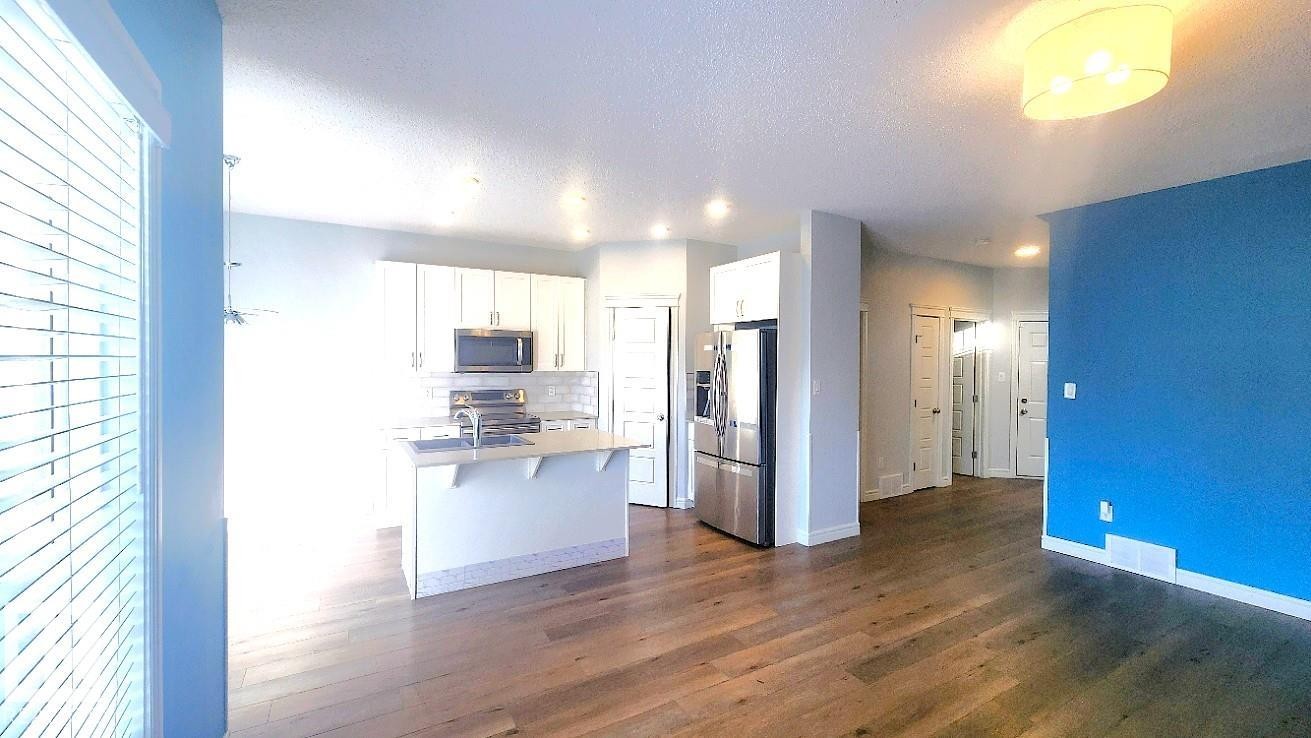 Kitchen with white cabinets, appliances with stainless steel finishes, an island with sink, dark wood finished floors, and light countertops - 4610 Kinsella Landing Sw, Edmonton, AB - Indoor Photo Showing Kitchen