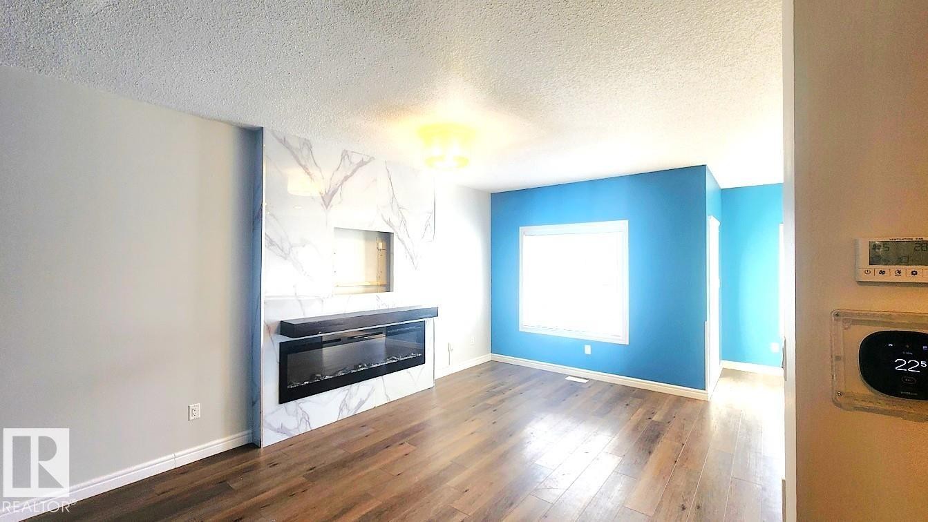 Unfurnished living room featuring a glass covered fireplace, dark wood-type flooring, and a textured ceiling - 4610 Kinsella Landing Sw, Edmonton, AB - Indoor Photo Showing Other Room With Fireplace