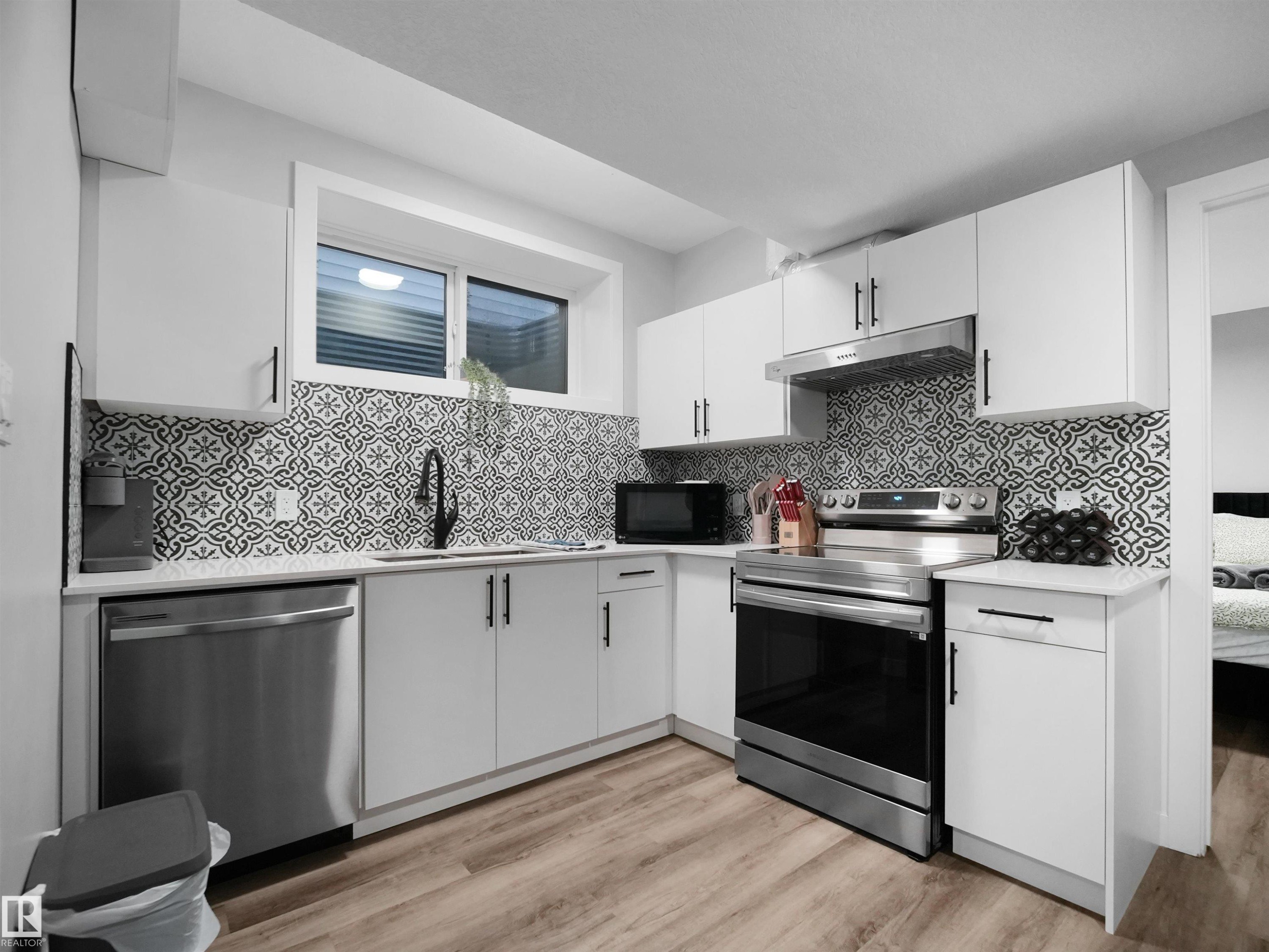 Kitchen featuring appliances with stainless steel finishes, white cabinetry, under cabinet range hood, light wood finished floors, and light stone counters - 10911 159 Street, Edmonton, AB - Indoor Photo Showing Kitchen With Upgraded Kitchen