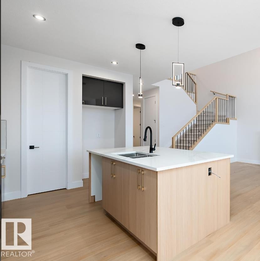 Kitchen featuring modern cabinets, light wood-type flooring, hanging light fixtures, light brown cabinetry, and an island with sink - 38 Astoria Place, Devon, AB - Indoor Photo Showing Kitchen With Double Sink