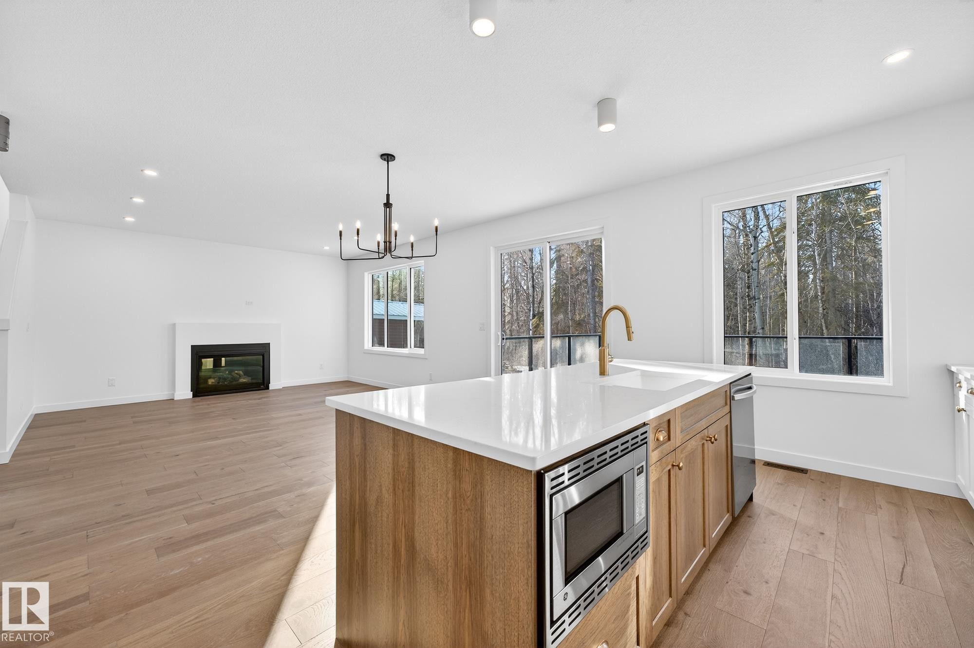 Kitchen with recessed lighting, light wood-type flooring, a center island with sink, pendant lighting, and stainless steel appliances - 132 Heron Point Close, Rural Wetaskiwin County, AB - Indoor Photo Showing Kitchen With Fireplace