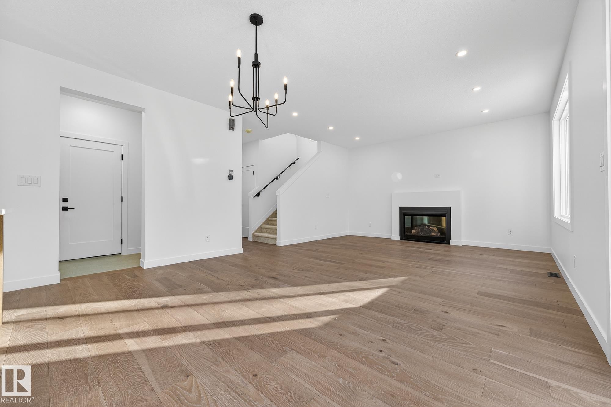 Unfurnished living room with a glass covered fireplace, a chandelier, stairs, light wood-style flooring, and recessed lighting - 132 Heron Point Close, Rural Wetaskiwin County, AB - Indoor With Fireplace