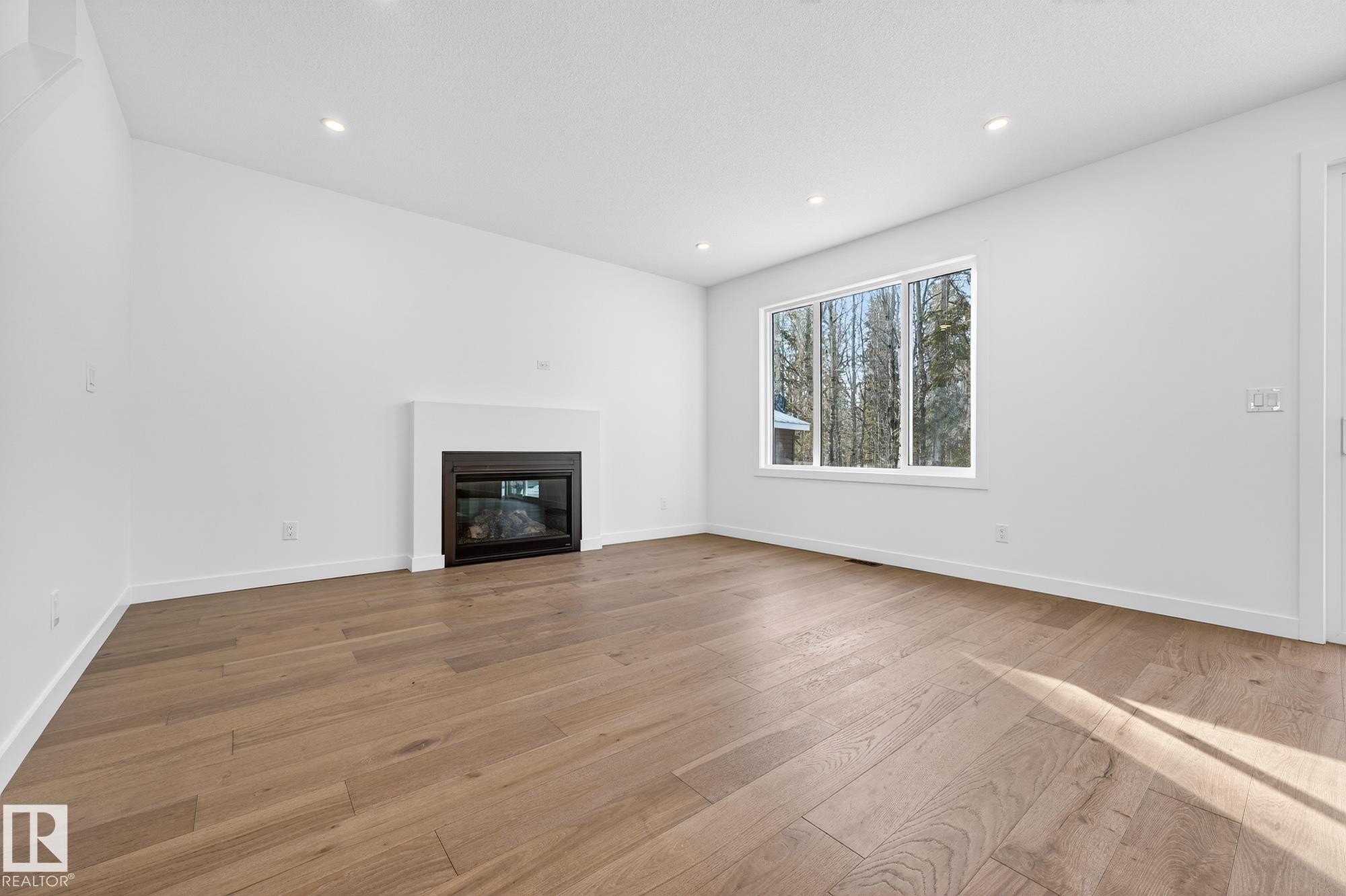 Unfurnished living room with a glass covered fireplace, light wood-style floors, and recessed lighting - 132 Heron Point Close, Rural Wetaskiwin County, AB - Indoor Photo Showing Living Room With Fireplace