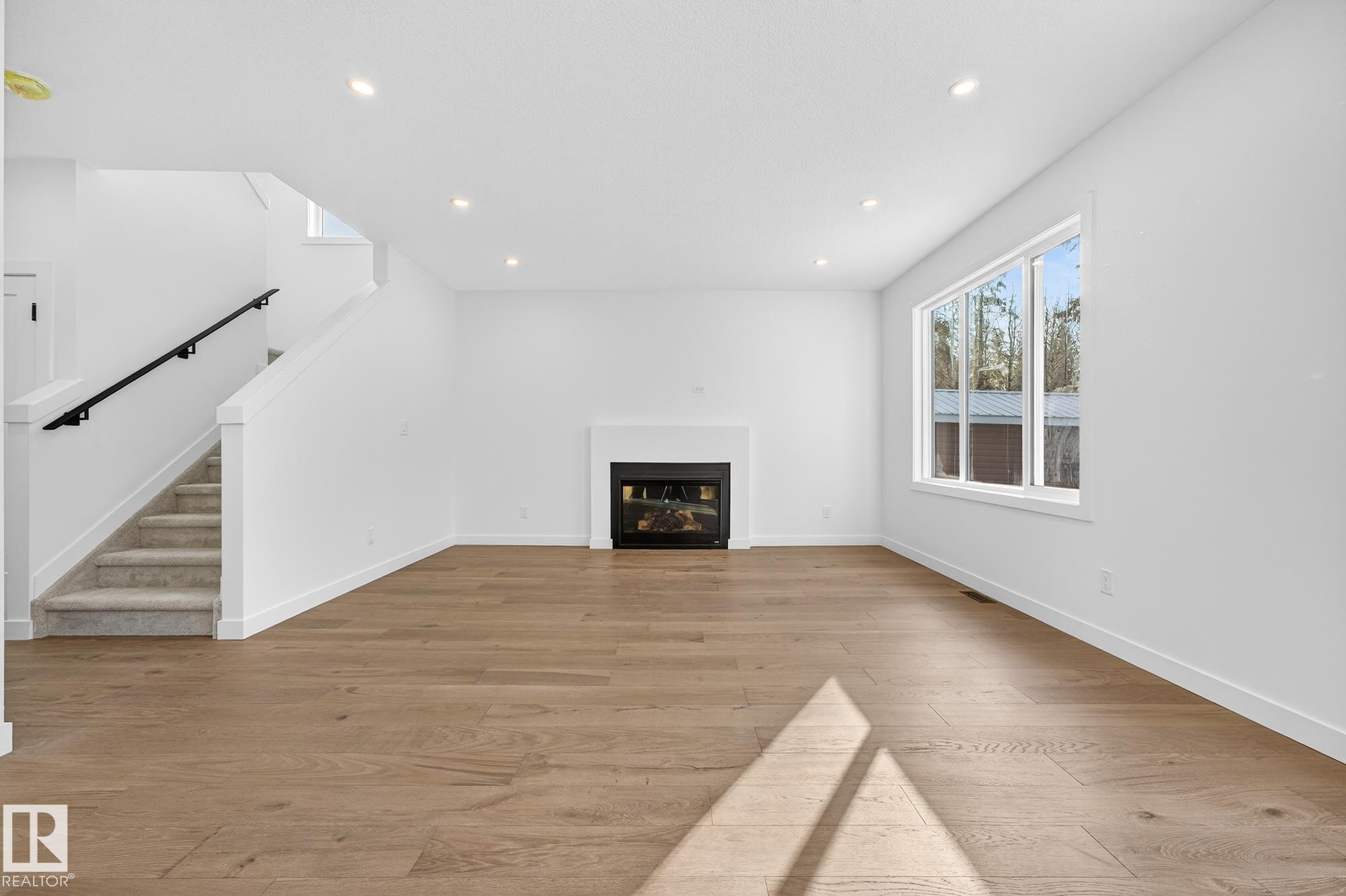 Unfurnished living room featuring stairway, light wood-style floors, a glass covered fireplace, and recessed lighting - 132 Heron Point Close, Rural Wetaskiwin County, AB - Indoor Photo Showing Other Room With Fireplace