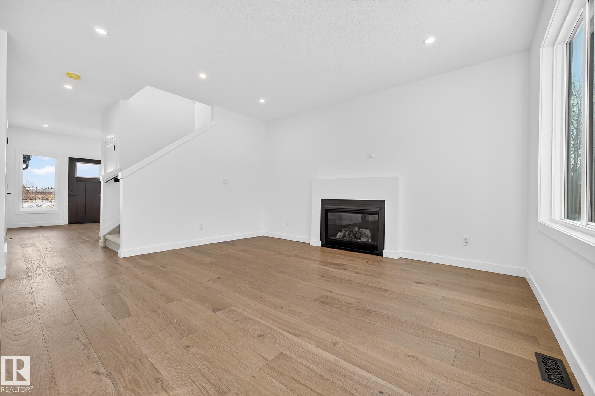 Unfurnished living room with light wood finished floors, a glass covered fireplace, stairway, and recessed lighting - 132 Heron Point Close, Rural Wetaskiwin County, AB - Indoor Photo Showing Living Room With Fireplace