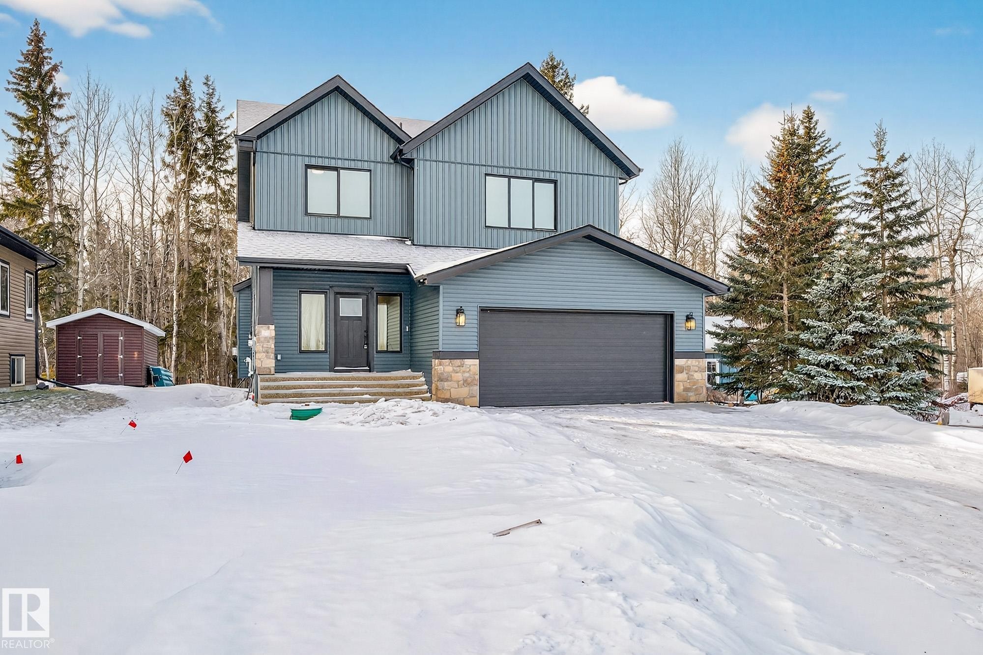 View of front of property featuring a garage, stone siding, board and batten siding, and a storage shed - 132 Heron Point Close, Rural Wetaskiwin County, AB - Outdoor With Facade