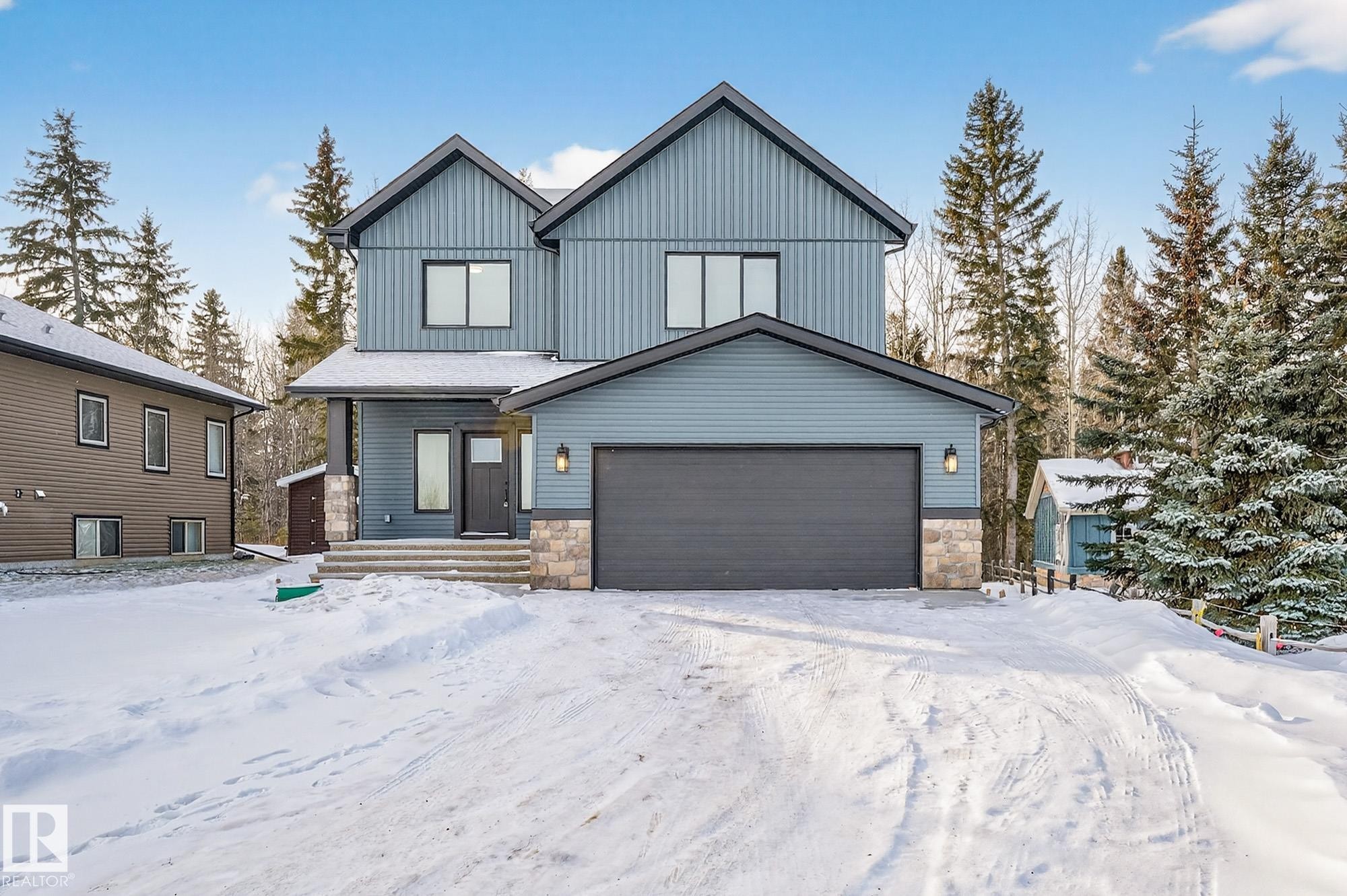 View of front of property with stone siding, a garage, and board and batten siding - 132 Heron Point Close, Rural Wetaskiwin County, AB - Outdoor With Facade