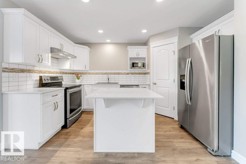 Kitchen featuring stainless steel appliances, white cabinetry, a center island, under cabinet range hood, and light wood-type flooring - 1423 24 Street, Edmonton, AB - Indoor Photo Showing Kitchen With Stainless Steel Kitchen With Upgraded Kitchen