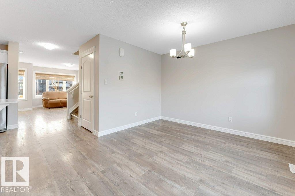 Unfurnished room featuring a chandelier, light wood-type flooring, stairs, and a textured ceiling - 1423 24 Street, Edmonton, AB - Indoor Photo Showing Other Room