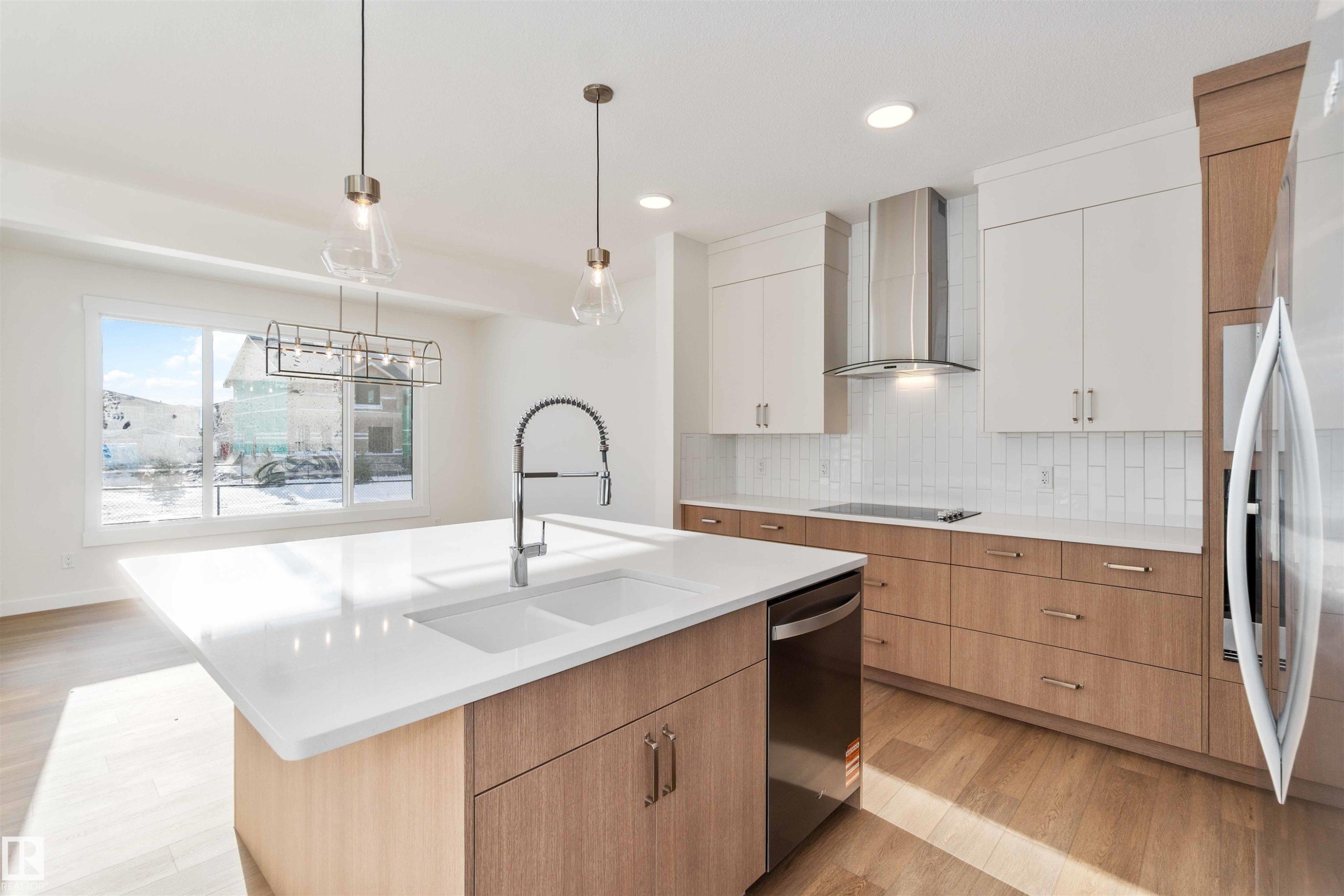 Kitchen featuring light wood-type flooring, an island with sink, decorative backsplash, wall chimney exhaust hood, and freestanding refrigerator - 2215 4 Avenue, Edmonton, AB - Indoor Photo Showing Kitchen With Upgraded Kitchen