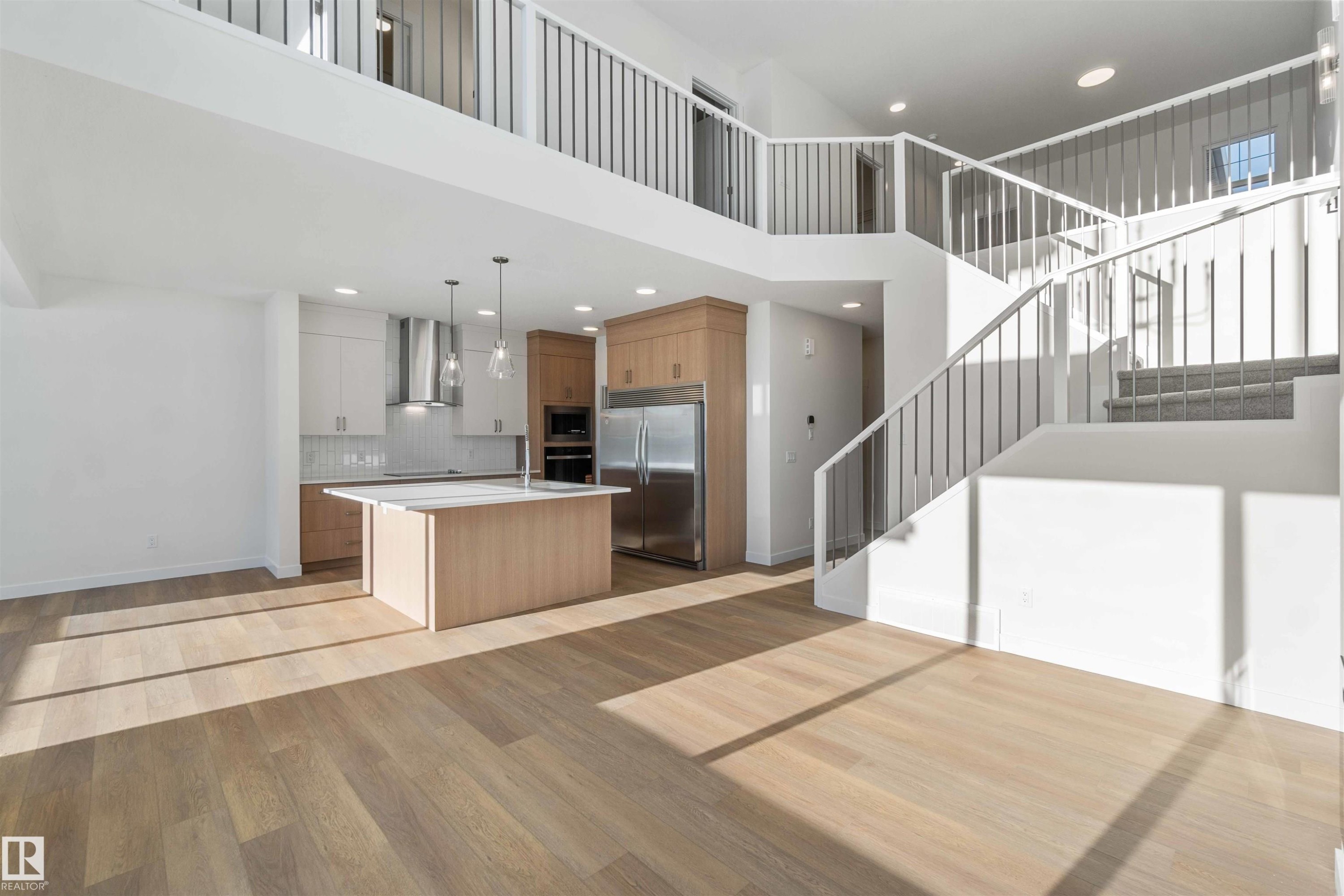 Kitchen with an island with sink, modern cabinets, black appliances, a high ceiling, and light wood-type flooring - 2215 4 Avenue, Edmonton, AB - Indoor Photo Showing Kitchen