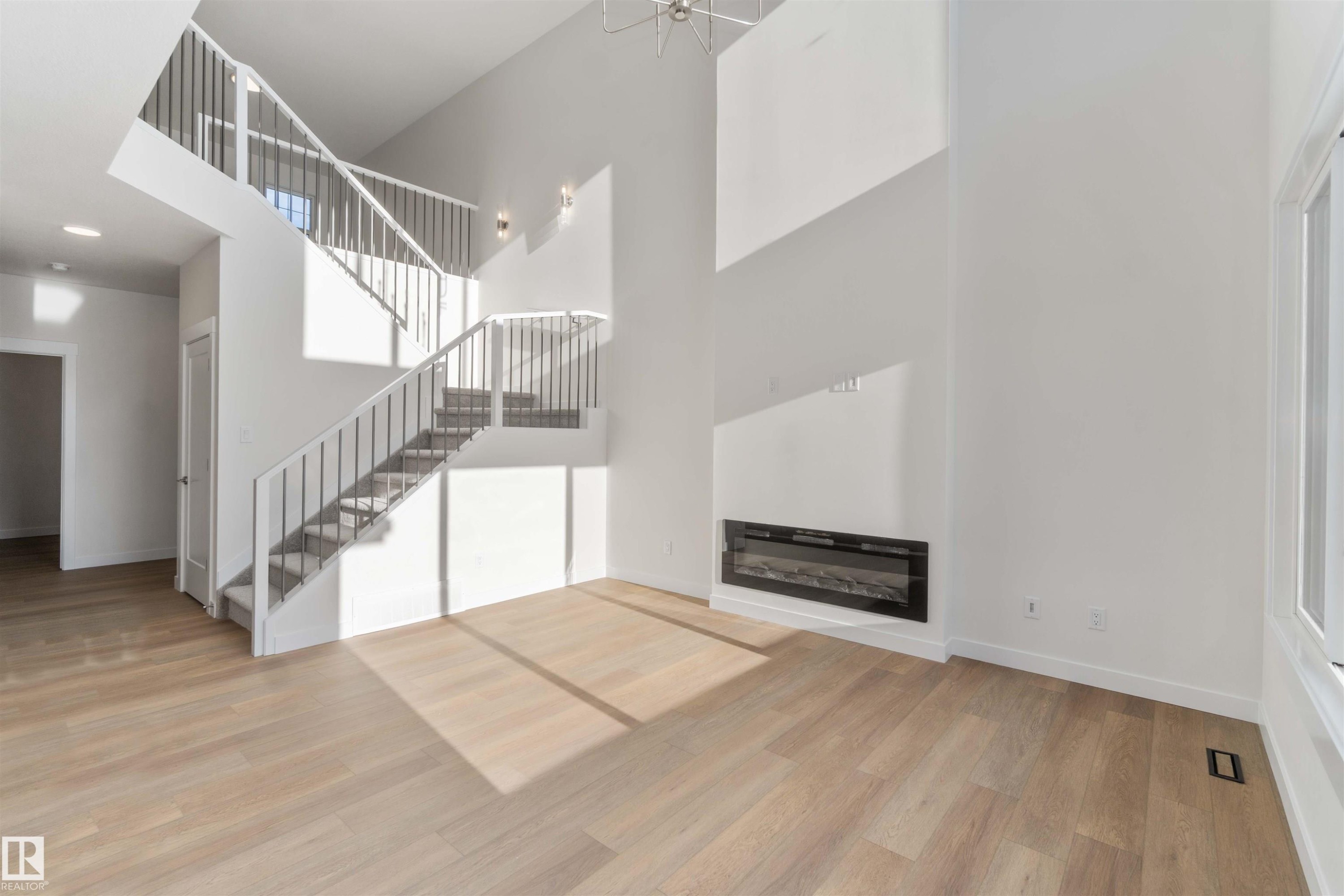 Unfurnished living room with light wood-style floors, a high ceiling, a glass covered fireplace, and stairway - 2215 4 Avenue, Edmonton, AB - Indoor With Fireplace
