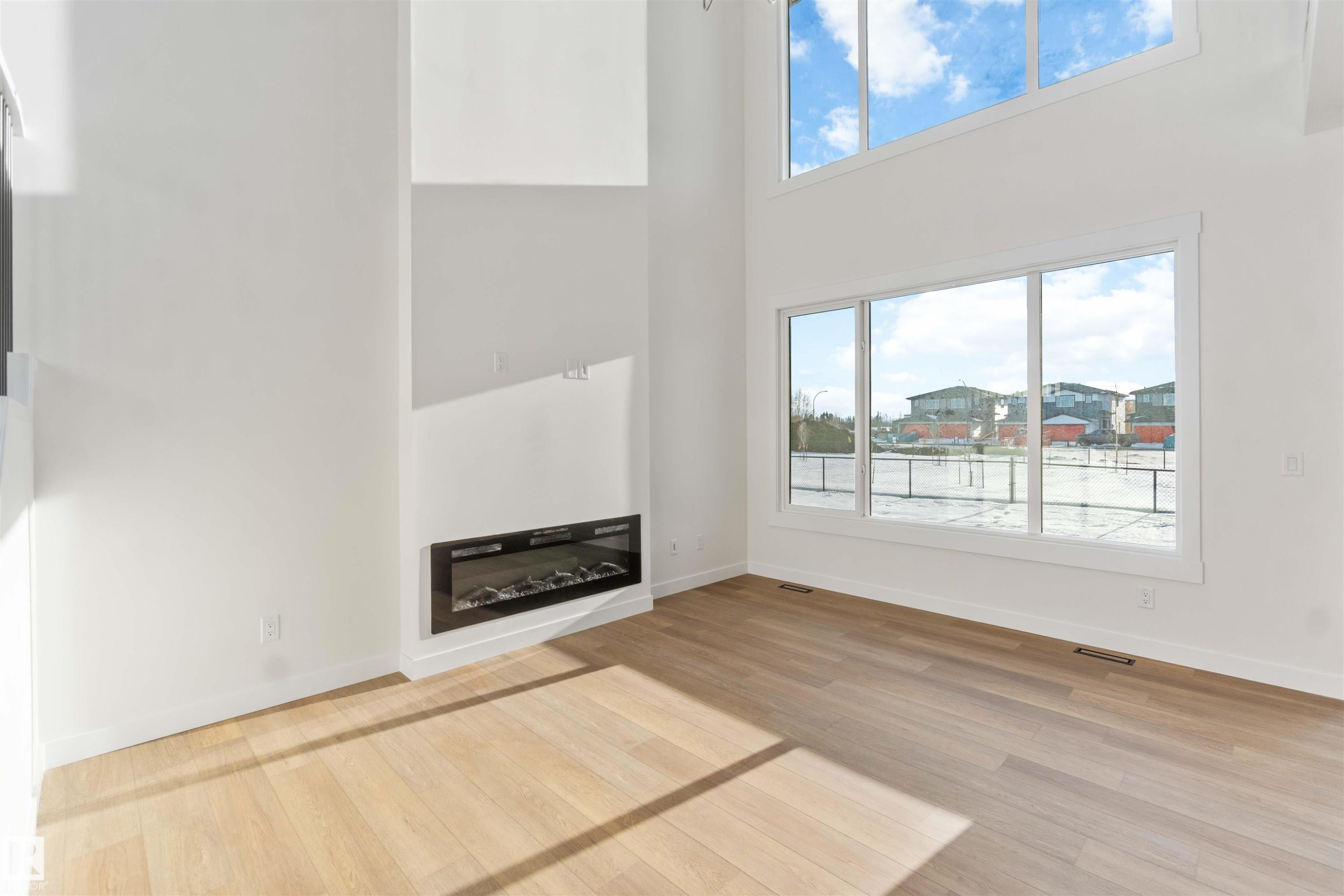 Unfurnished living room with a towering ceiling, plenty of natural light, light wood-style flooring, and a glass covered fireplace - 2215 4 Avenue, Edmonton, AB - Indoor With Fireplace
