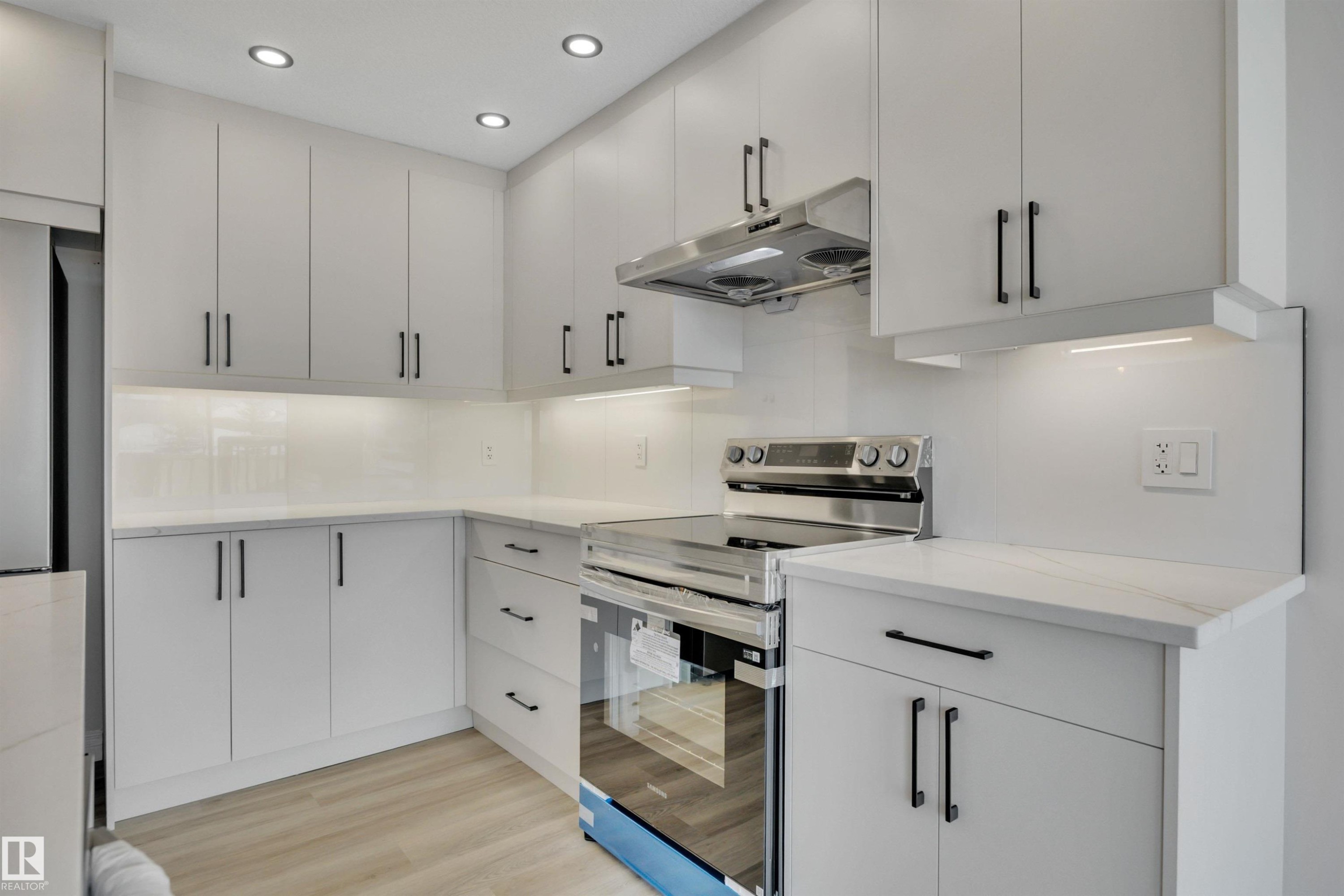 Kitchen featuring stainless steel electric stove, under cabinet range hood, light wood finished floors, recessed lighting, and white cabinets - 457 Aster Close, Leduc, AB - Indoor Photo Showing Kitchen With Upgraded Kitchen
